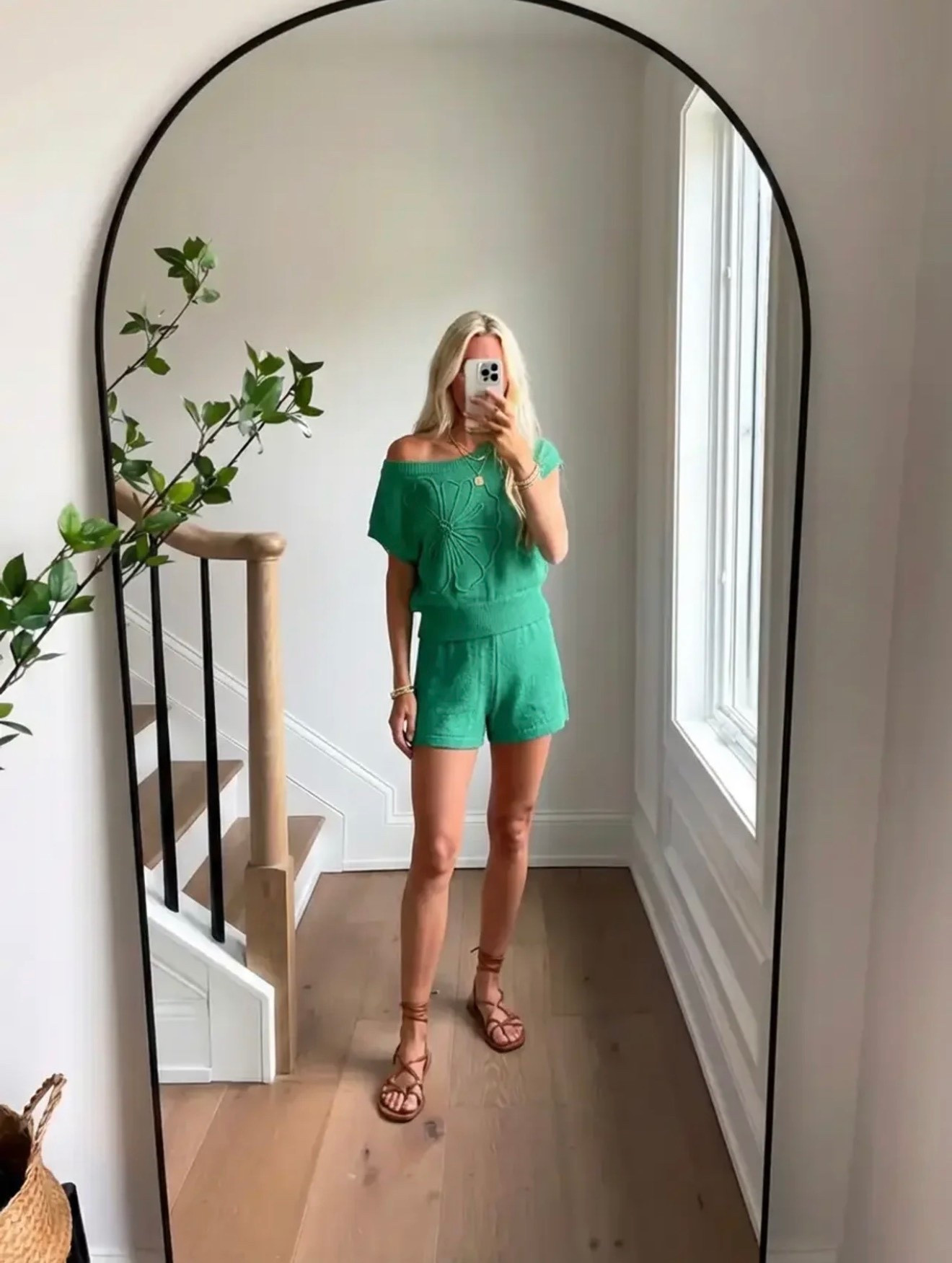 A bright lifestyle fashion mirror selfie inside a modern home. A woman with long blonde hair stands in front of a large arched black-framed mirror wearing a vibrant green off-the-shoulder knit top with matching green shorts, styled with brown lace-up flat sandals and delicate gold jewelry. The interior features light oak wood flooring, white walls, a staircase with a natural wood railing and black metal balusters, and soft natural daylight streaming through a tall window. A leafy green plant branch adds an organic touch. The aesthetic is fresh summer style, effortless vacation fashion, coastal modern minimalism, natural light lifestyle photography.

Caption

A little color, a little sunshine, and summer feels. 💚

Hashtags

#SummerStyle
#ResortStyle
#VacationOutfit
#EffortlessStyle
#CasualChic
#GreenOutfit
#SummerOutfitIdeas
#MirrorSelfieStyle
#CoastalStyle
#TravelStyle
#OOTDInspo
#StyleInspoDaily
#CasualLuxury
#ChicAndSimple
#EverydayStyle
#StyleInfluencer
#SummerWardrobe
#ResortWear
#VacationVibes
#EasySummerStyle

#LTKgrwm #LTKdayinmylife #LTKSpringSale