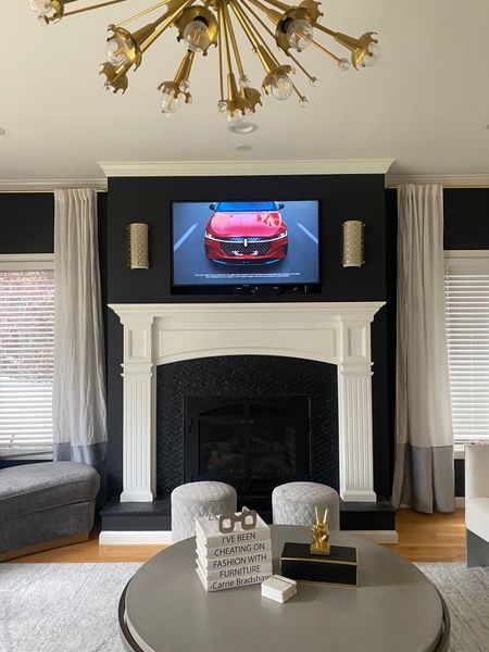 Frame TV over the mantle with black accent wall so it blends right in. Grey velvet ottomans and gold chandelier for the win! 

#LTKHome #LTKOver40 #LTKStyleTip