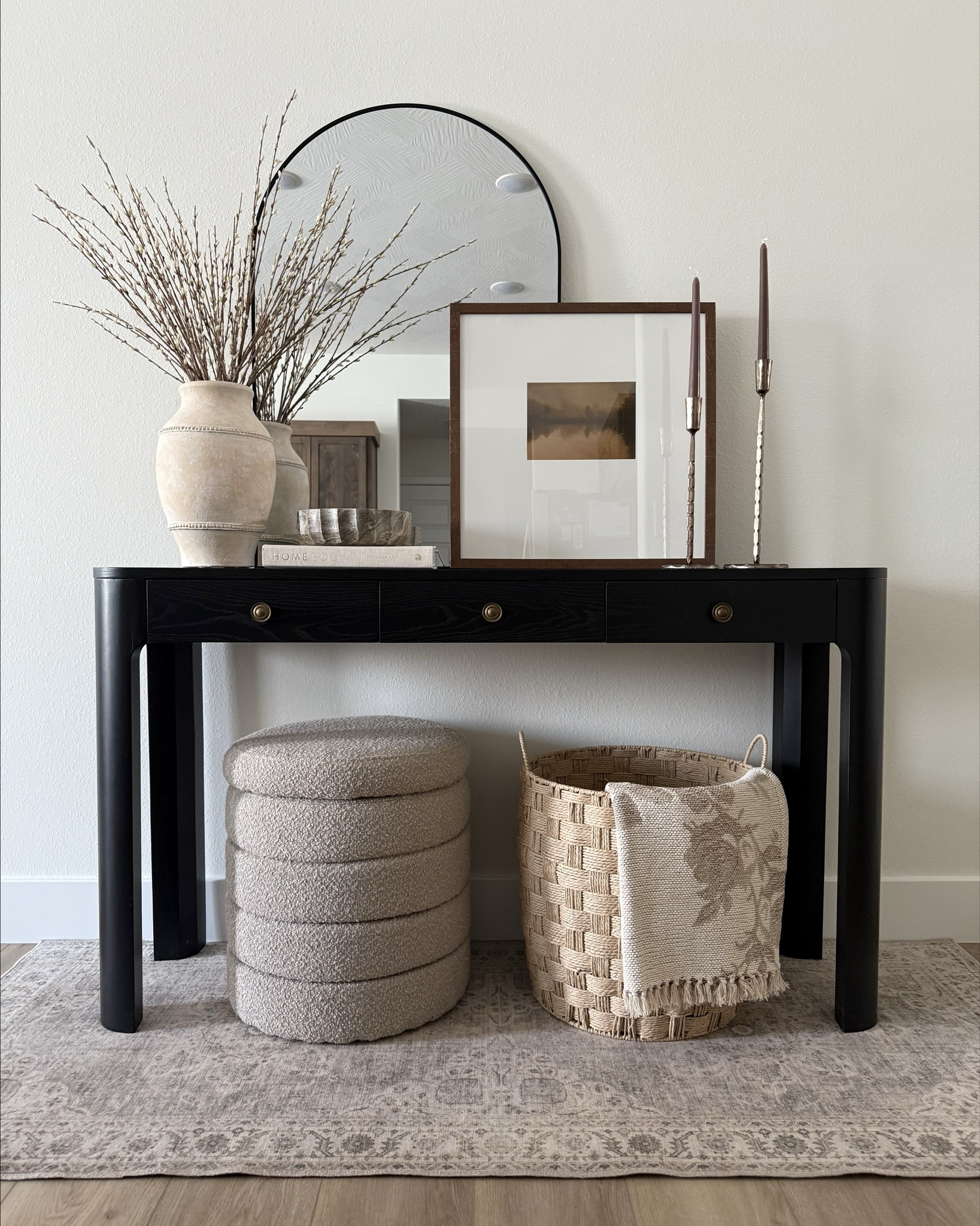This black console table instantly grounds the whole space and gives the entry such a polished, designer feel. I love the soft curved edges, warm brass knobs, and how the dark finish lets neutral decor really stand out. Styling it with layered art, warm wood tones, and textured pieces keeps it feeling simple but elevated—one of those spots in the home that just feels good every time you walk by.

#LTKHome