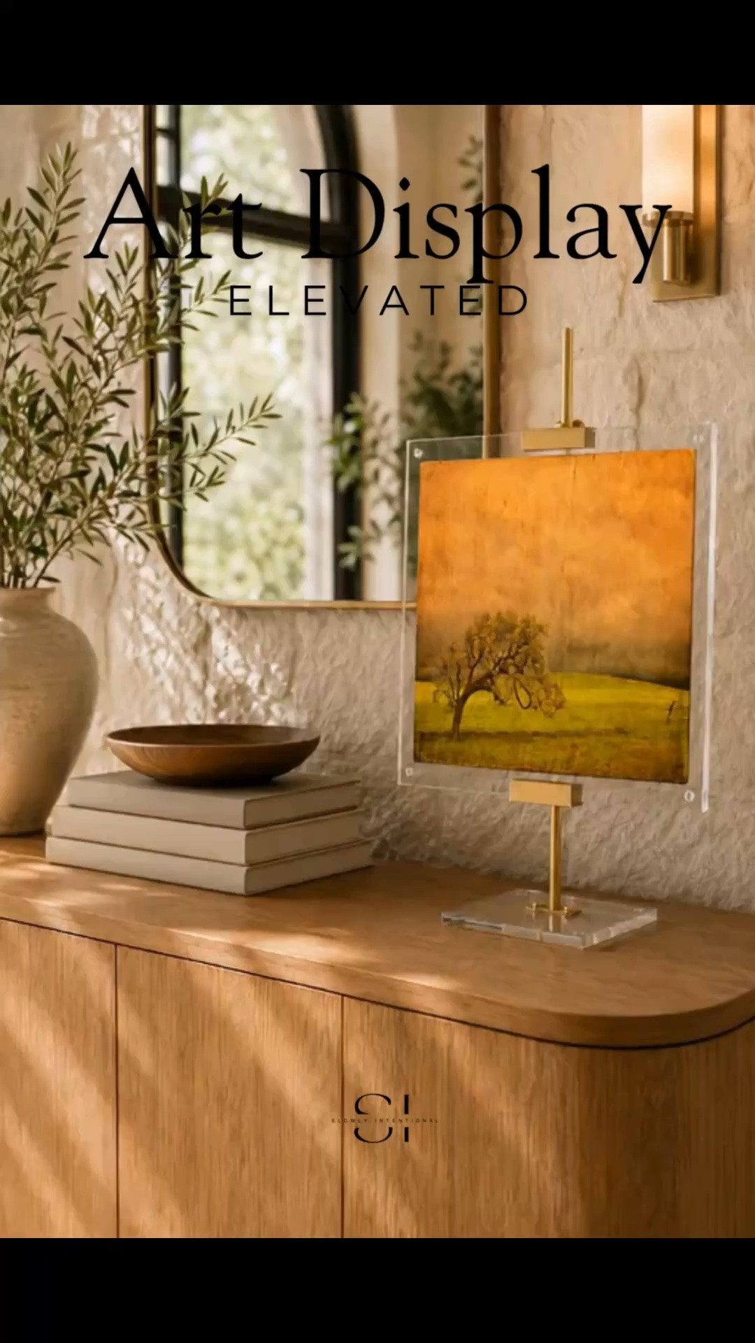Tabletop art easel styling idea for an organic modern home. This warm console table vignette features an acrylic art display, brass easel hardware, neutral textures, wood tones, greenery, and soft golden light for a polished gallery-inspired look. Save this acrylic art easel decor idea for elevated home styling inspiration. Amazon finds, artwork display