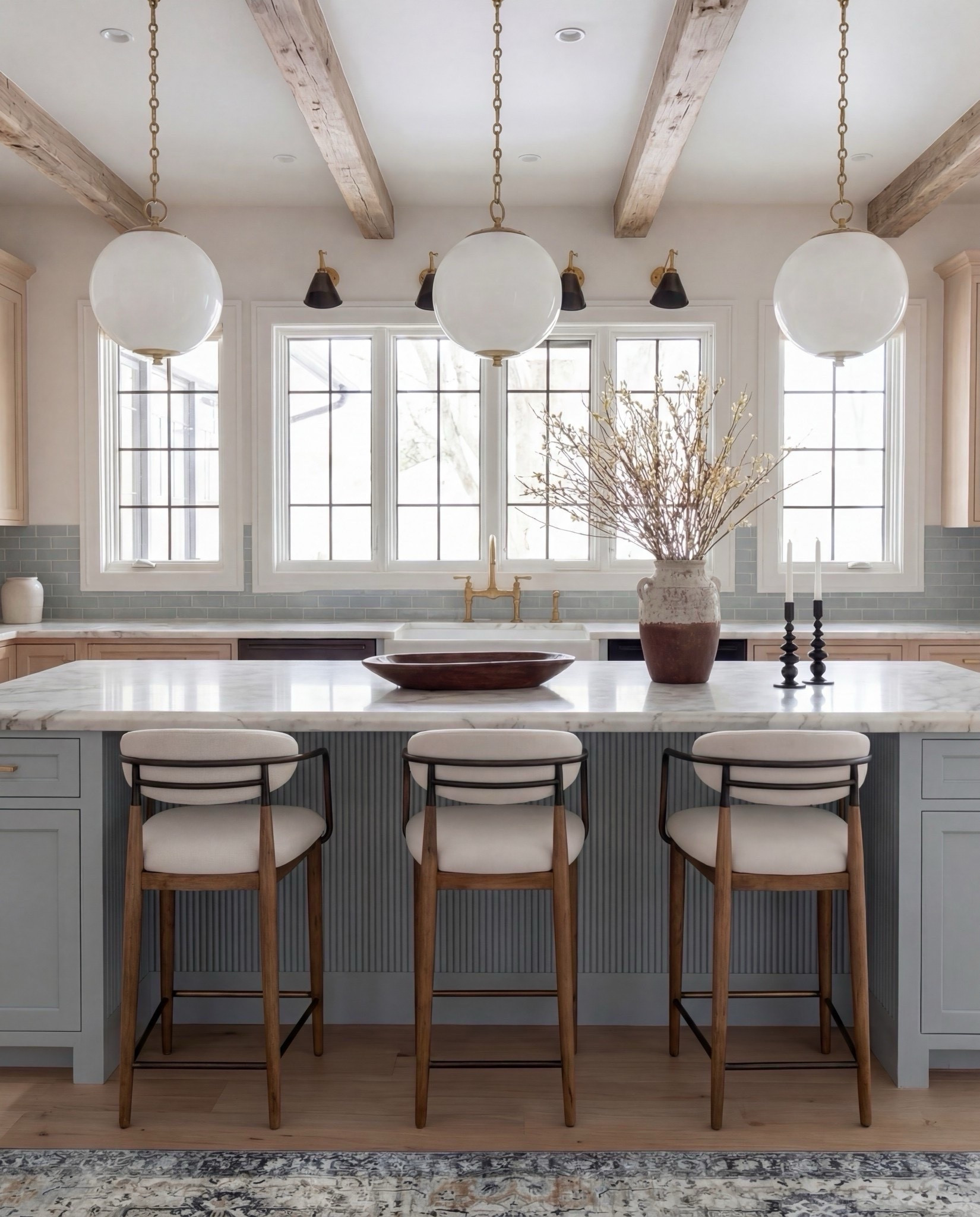 Shop the Look:
• Light blue fluted kitchen island
• Warm oak kitchen cabinets
• Brass globe pendant lights
• Marble kitchen countertop
• Neutral blue patterned runner
• Black + brass bar stools
• Soft blue subway tile backsplash
• Brown Ceramic vase with branches
• Gold kitchen faucet and hardware
•Brown bowl 
Brown floral wall art
Black candle holder

#LTKHome #LTKSaleAlert