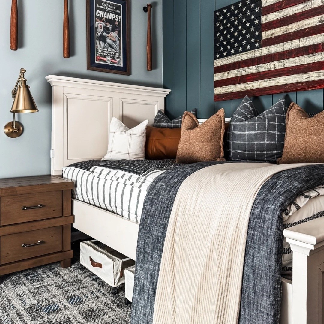 All-American bedroom style 🇺🇸 This space features a classic white bed frame with striped bedding, layered throw blankets, and cozy accent pillows in plaid, leather, and neutral tones. A wooden nightstand with a brass wall sconce adds warmth, while the framed sports poster, baseball bats as wall decor, and American flag artwork bring personality. Finished with under-bed storage and a patterned rug for function + style. ⚾️

Bedding by Beddy’s
Code EANES = 20% off 

Bedding Details: 
Chandler Beddy’s (Twin, Cotton, ZipBase)
Taylor Luxe Blanket 
On-the-go blanket tan grid 
Owen Luxe Leather XL Lumbar Pillow Cover
Lincoln Medium Pillow Cover
Monroe Medium Pillow Cover 
Lucas Euro Pillow Cover


#BedroomDesign #AllAmericanStyle #StripedBedding #ThrowBlankets #AccentPillows #WoodNightstand #BrassSconce #SportsPoster #BaseballDecor #AmericanFlagArt #UnderBedStorage #PatternedRug #eanesinteriors


#LTKHome #LTKStyleTip #LTKOver40