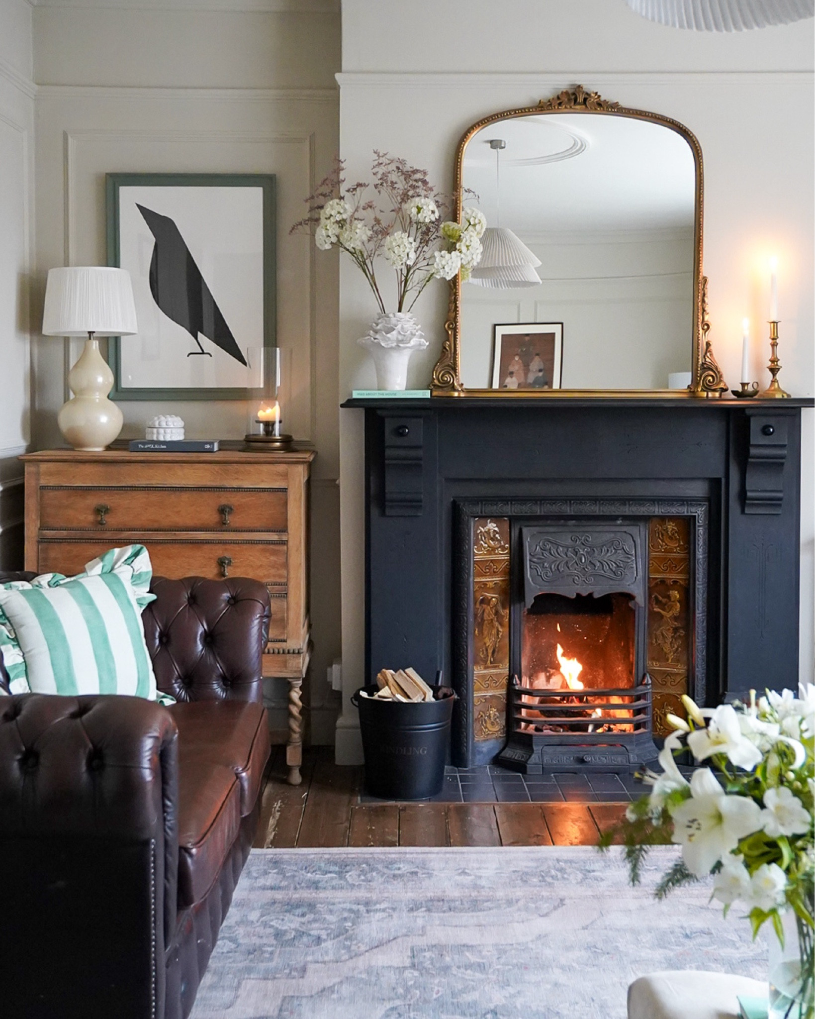 Traditional period living room with large gold over mantle mirror, white vase, white urn lamp, green stripe ruffle cushion and washable rug. 

#LTKover40 #LTKhome #LTKeurope