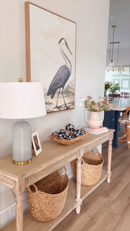 Coastal front entry way. Great blue heron vintage art reproduction canvas with wood frame. Blue table lamp, vase, pink flowers florals, pink coffee table book, white coffee table book, sea grass baskets for storage, console, woven entry bench, black metal frame with white mat, garden stool, faux monsterra plant, throw pillows  

#LTKhome