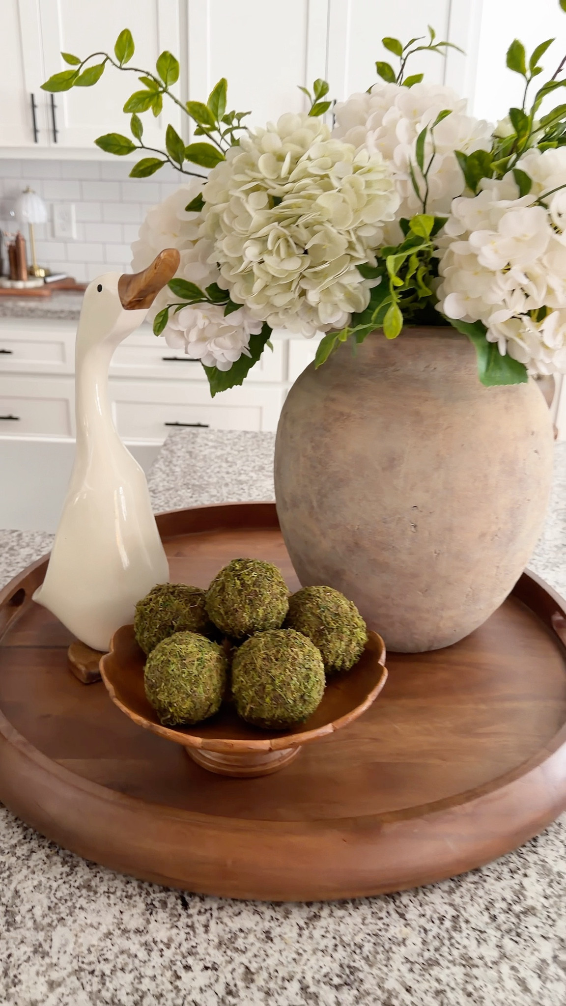 Such a beautiful look for an island or dining table centerpiece. I used real touch hydrangeas paired with a little greenery to give it some height and fullness. A scalloped wood bowl filled with moss balls adds the cutest duck/goose you have ever seen! . 