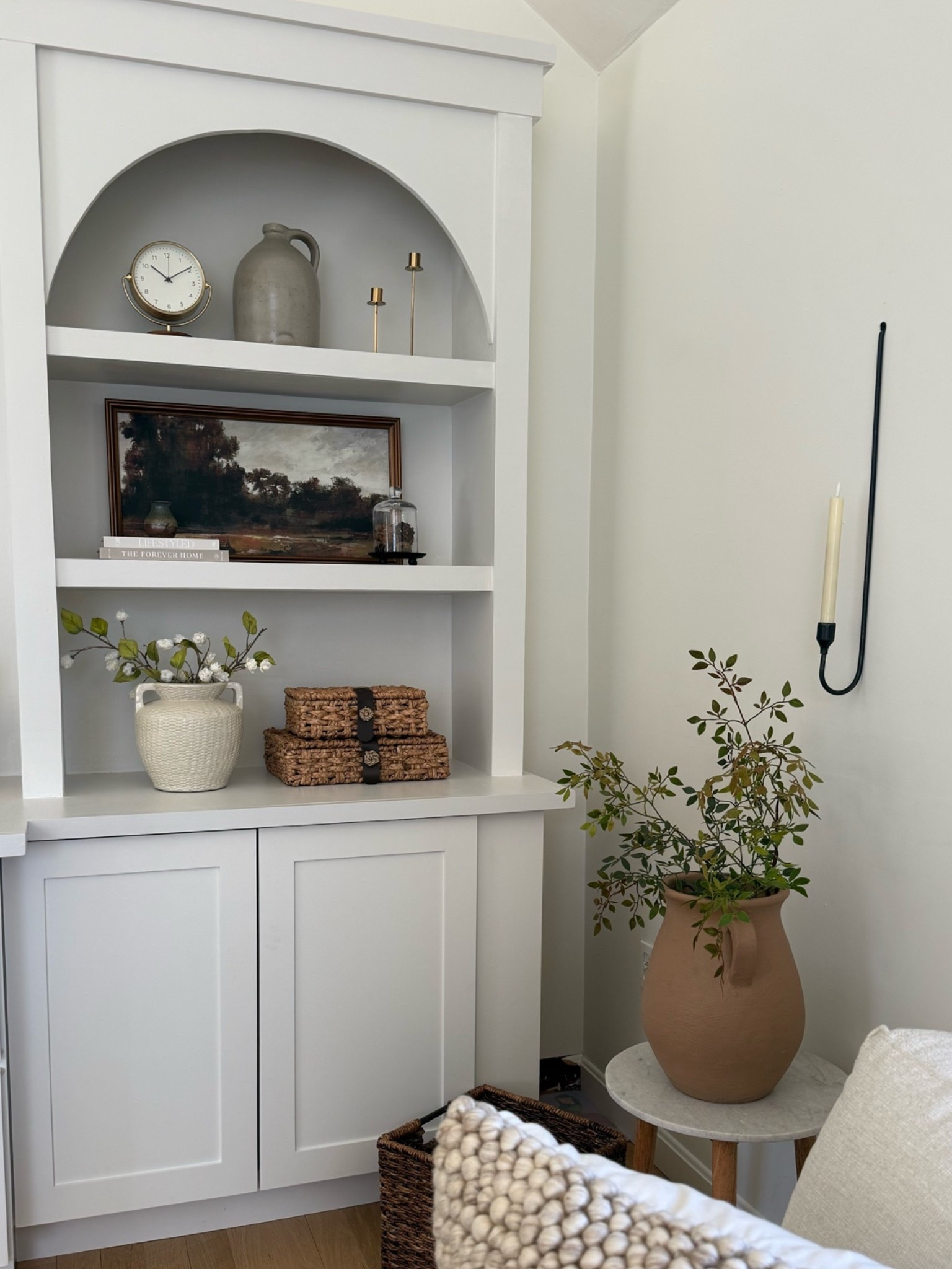 Shelf styling in the corner of our family room. I love using landscape art to help fill in space in this one is currently on Clarence a beautiful vase with some color and some greens. Add more texture and color and of course my favorite wall candle sconces holder.