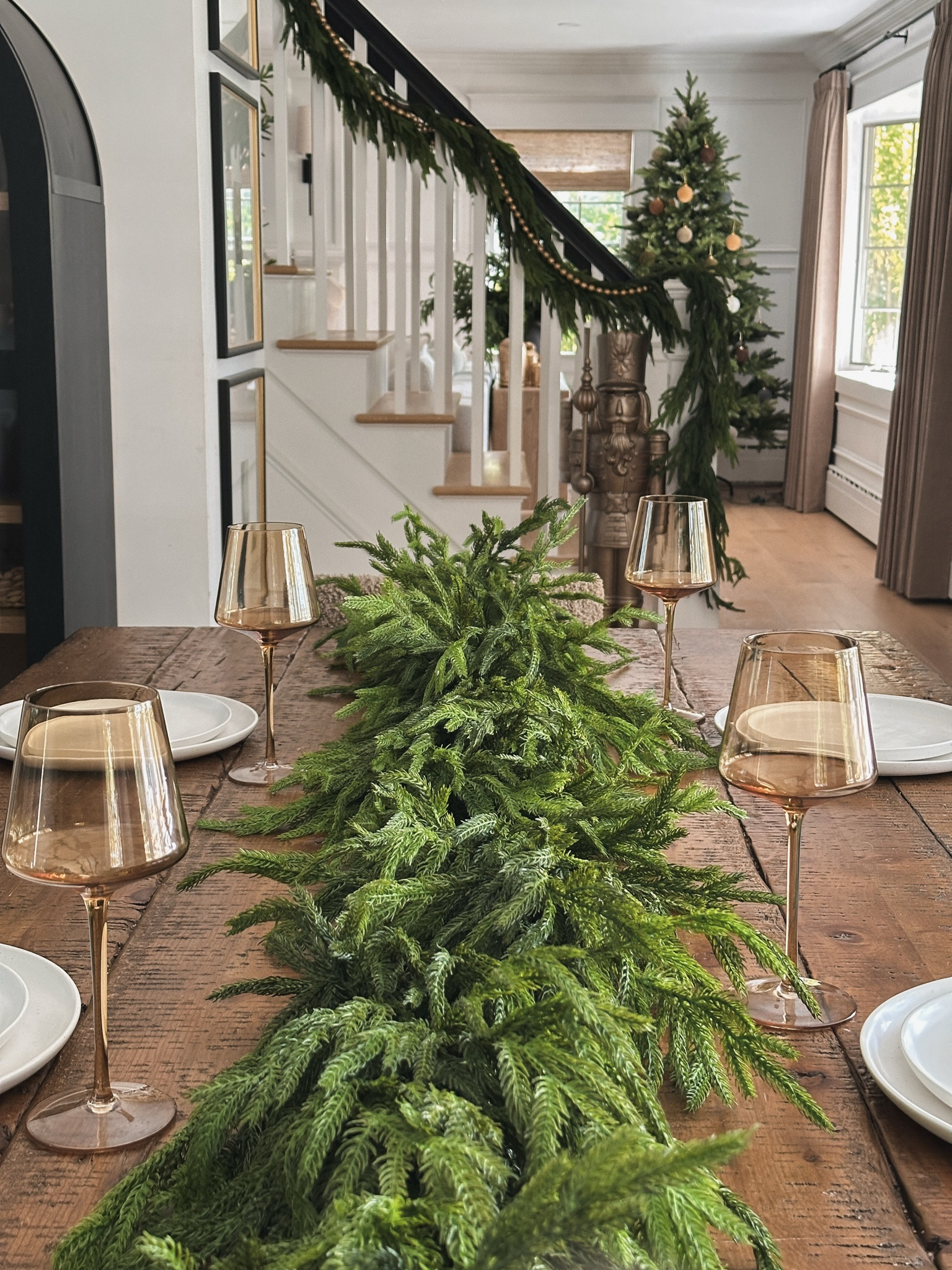Here’s a simple yet beautiful dining room tablescape. I utilized this fuller, deluxe artificial Norfolk garland, amber wine glasses, and flat dinnerware. I added the original garland to my staircase along with wood bead garland. My nutcracker statue is refinished with an antique bronze paint spray. You can also find my new Christmas tree decorating with velvety neutral flicked ornaments. 

Also shown: custom pinch pleat curtains in taupe grey and 20”x20” gallery frames.


#LTKHome #LTKSaleAlert #LTKHoliday