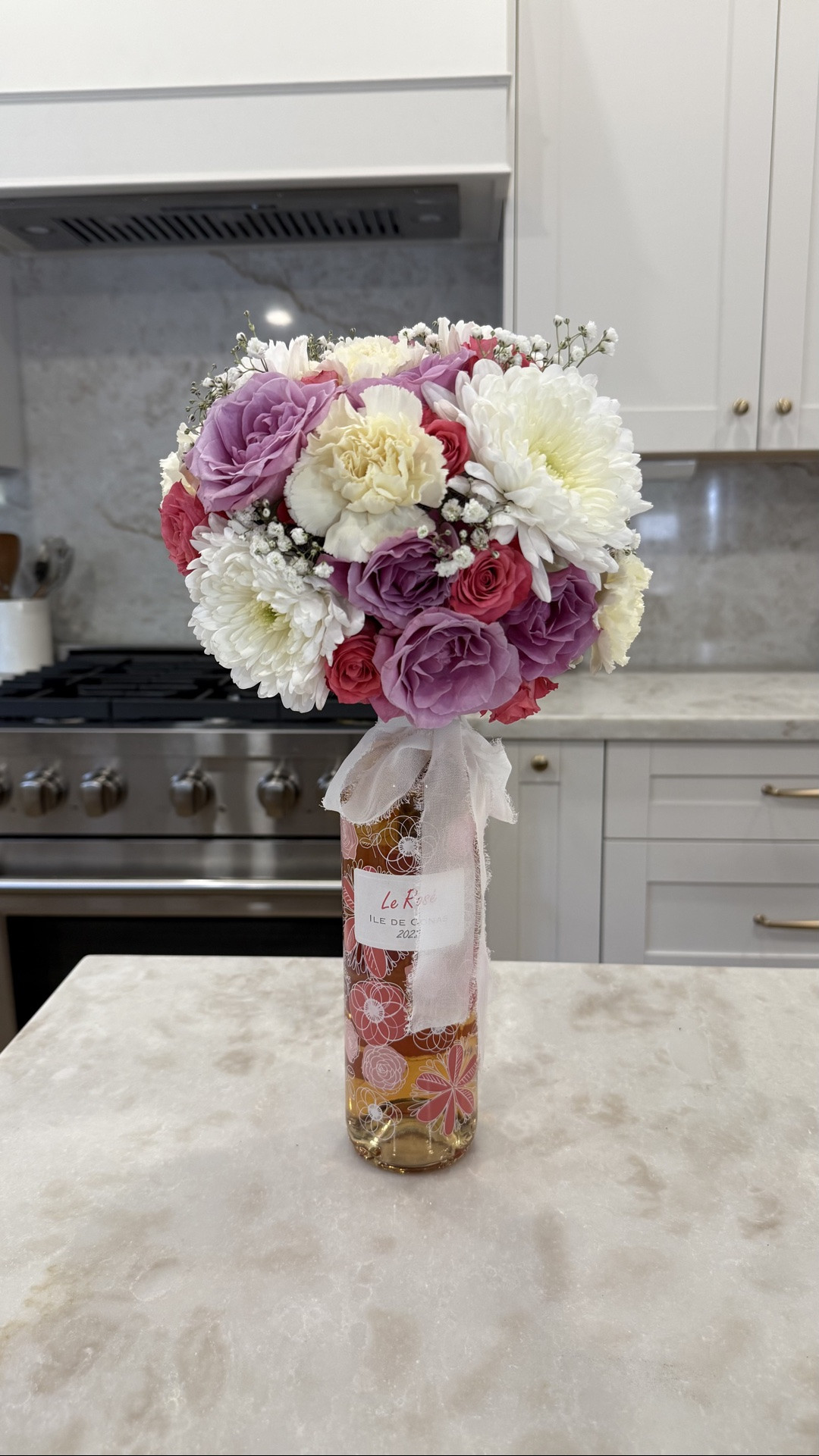 I love this flower arrangement idea for special occasions and it’s so perfect for Mother’s Day this weekend!! It comes together so easily and is sure to put a smile on her face. 

Take any wine bottle, I like this floral painted bottle from Trader Joe’s, and choose 3-4 bouquets of flowers. For this arrangement I went with pink and purple spray roses, white carnations, and white chrysanthemums. I also used some babies breathe as a filler. 💐

The trick is to use floral foam wrapped in plastic wrap so that it helps hold the water longer and doesn’t drip. Dont double up the plastic wrap or it will be difficult to get the stems to poke through. 

Then, just arrange as you wish!! I added a chiffon bow for an extra detail too. 

I hope this inspired you! Happy Mother’s Day! 🩷