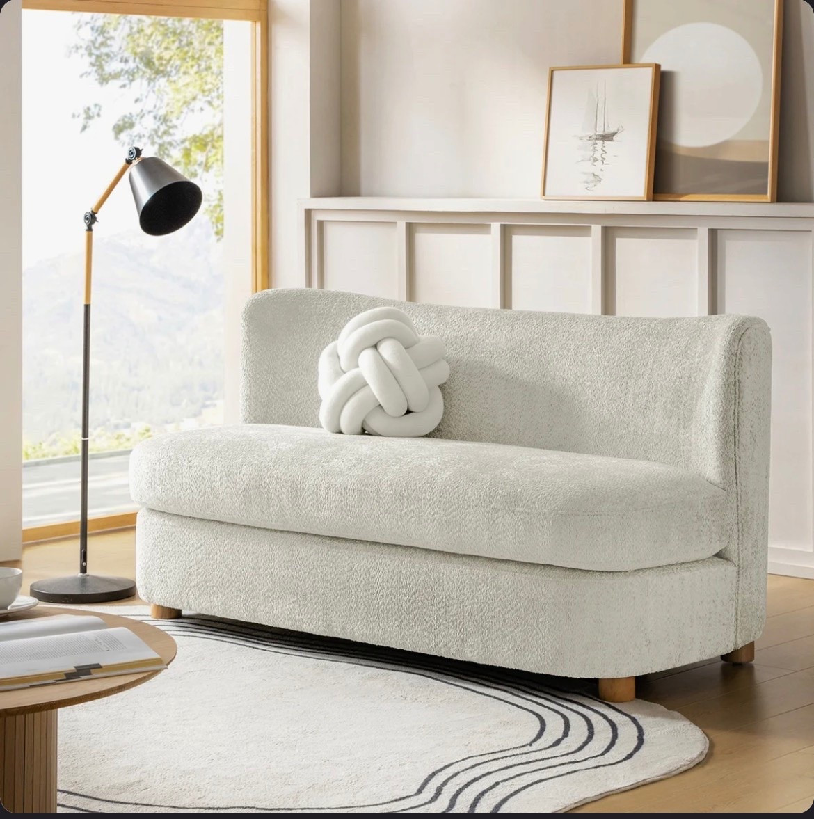 This 63-inch ivory boucle curved loveseat from Wayfair has such a soft, sculptural look. I love the rounded silhouette, textured upholstery, and cozy knot pillow for a small living room, apartment, or reading area. Styled with a black and wood floor lamp, round wood coffee table, neutral area rug, and simple framed wall art. #WayfairFinds #BoucleLoveseat #CurvedSofa #LivingRoomDecor