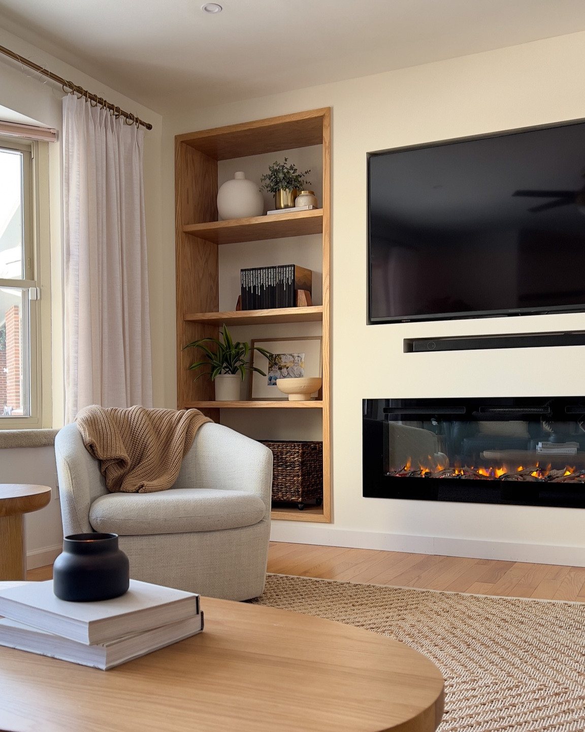 Cozy living room with built in TV and electric fireplace. Wood built-ins. Comfortable light grey swivel chair. Natural rug. Beige white curtains. Pleated drapes. Brass curtain rod. 

#LTKFind #LTKhome