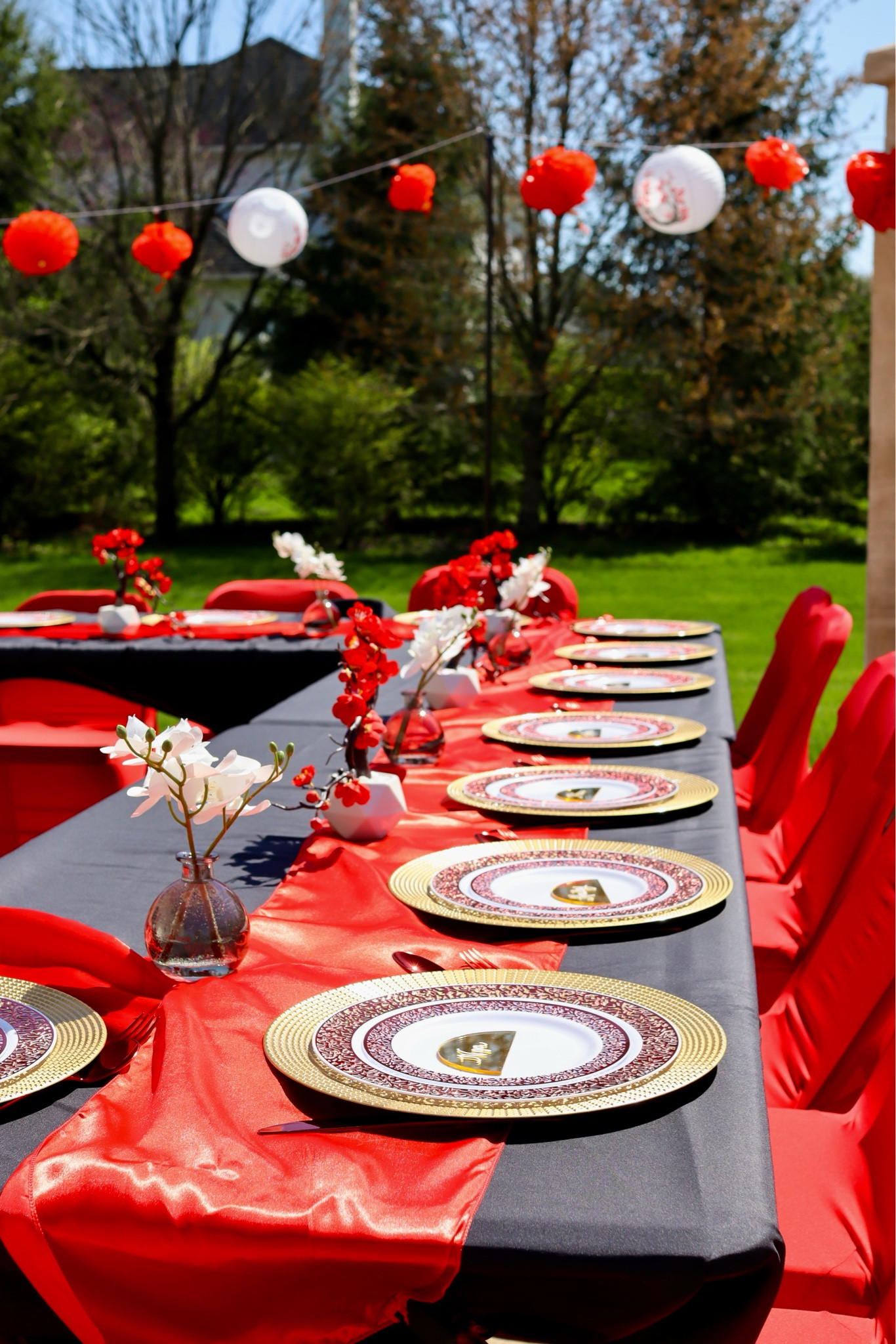 Outdoor Hibachi Party // Setting the scene with festive decor for an outdoor Hibachi party. The decorations included a tablescape with black tableclothes, red satin runner, gold chargers, red and white orchid plants, red chairs, and red and white lanterns stringed lanterns. On her was a navy blue romper with gold stitching.

#LTKhome #LTKSeasonal #LTKparties