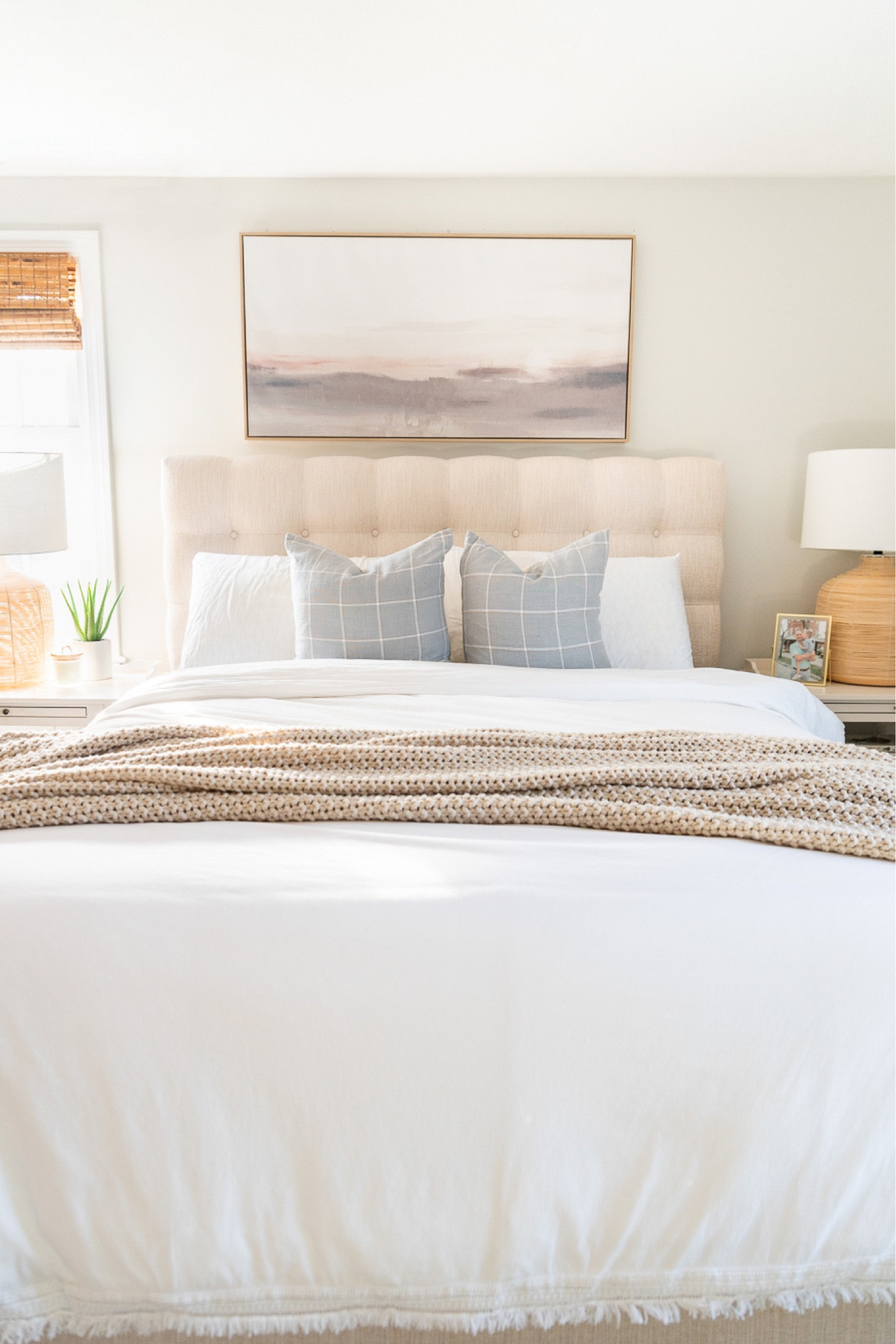 Spring bedroom decor featuring artwork, rattan table lamps, throw pillows and beautiful bedding. 