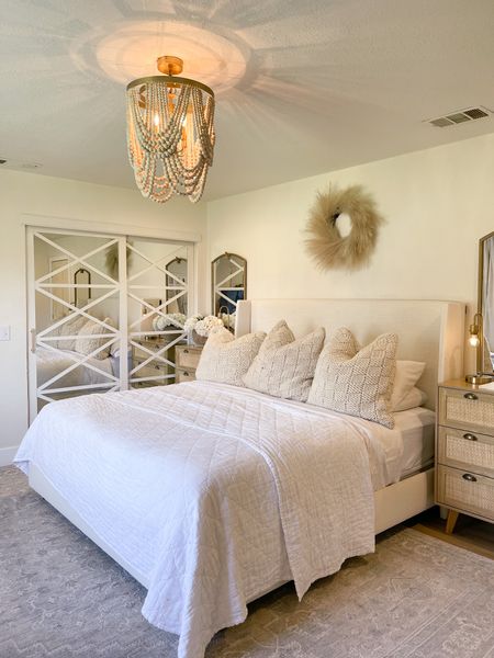 Primary bedroom organic modern white upholstered bed. Neutral area rug, closet doors cane rattan nightstand gold mirrors wood beaded chandelier. 


#LTKsalealert #LTKFind #LTKhome