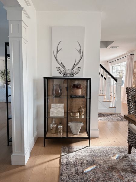 I love this beautiful, black and glass cabinet from IKEA. I added woodgrain adhesive paper to give it an elevated look. Similar cabinets go for 100s of dollars if not, thousands more. Shelf decor. Deer canvas art. 