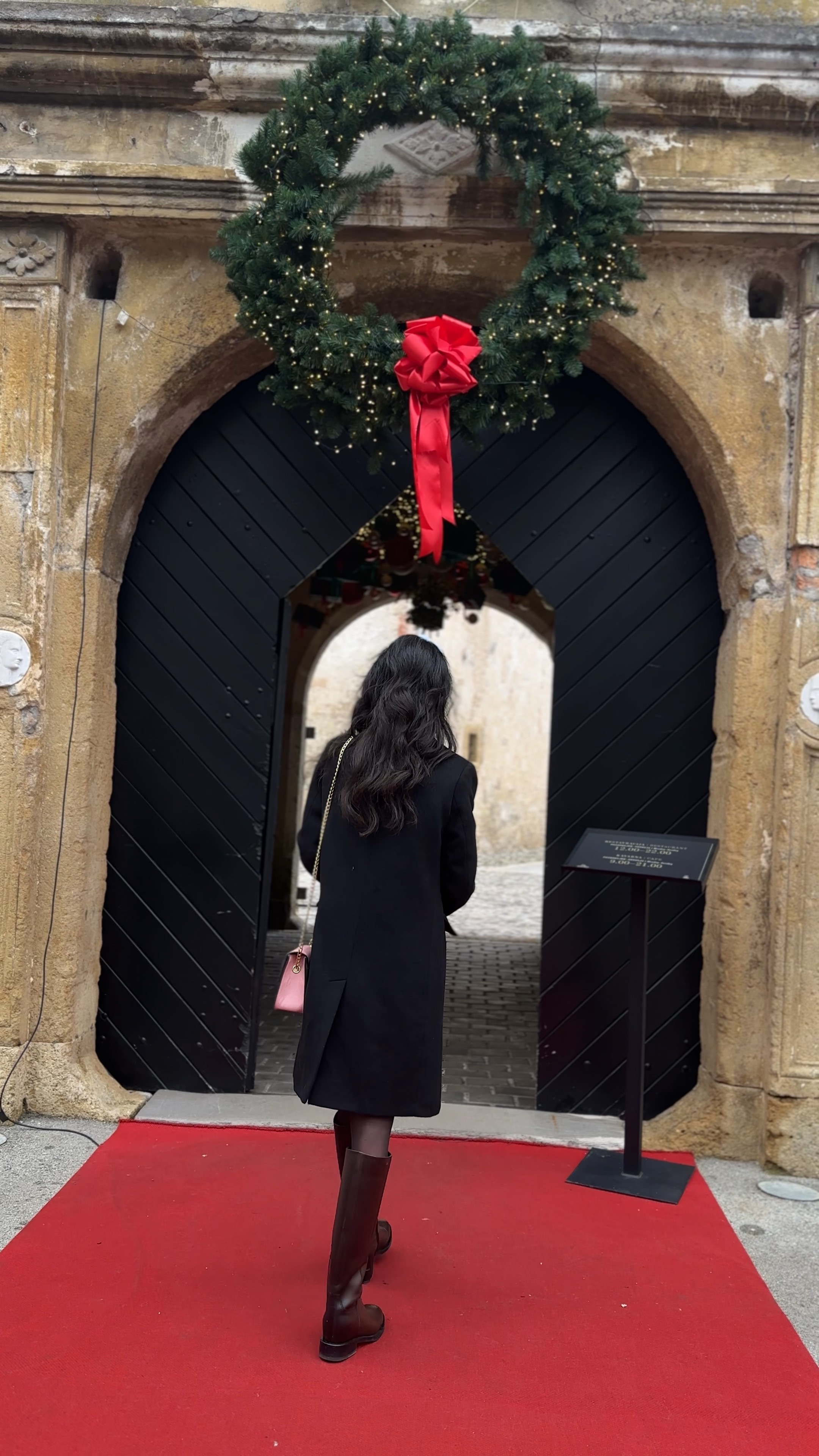 Christmas Eve outfits church, Christmas church outfit, black wool coat, Christmas wreath aesthetic, holiday outing look, brown riding boots, pink crossbody bag, festive winter fashion, elegant Christmas style, European Christmas, red bow wreath, winter coat outfit, Christmas tradition outfit, sophisticated holiday look, classic winter attire, church Christmas outfit, holiday occasion wear, timeless winter fashion, Christmas day outfit, festive arch entrance, elegant cold weather style 

 #LTKHoliday #LTKootd #LTKstorytime