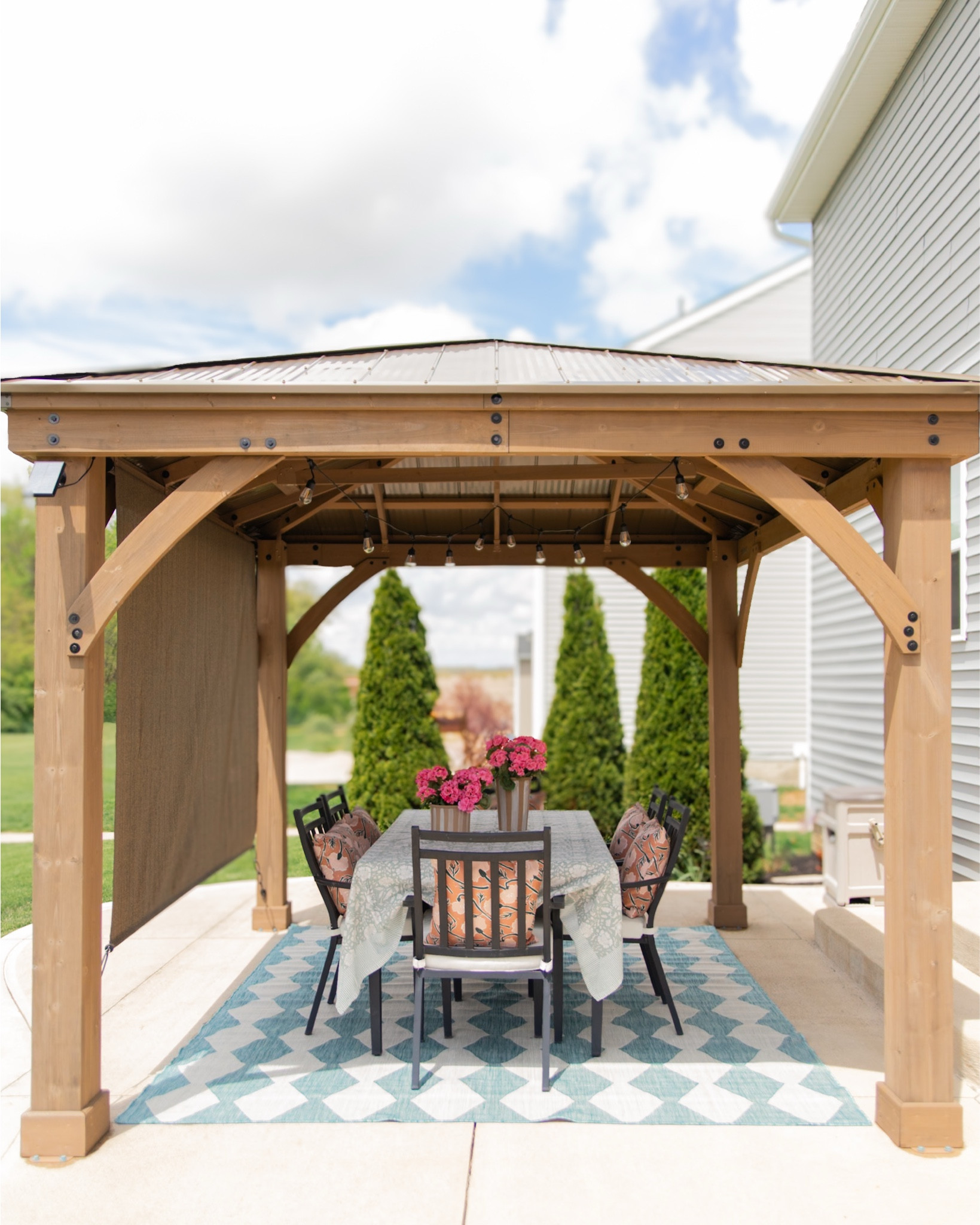 Another look at our patio makeover! I refreshed our basic concrete patio with a wooden gazebo, outdoor rug, hanging lights, roller shade, and table decorations to get ready for summer. @wayfair #wayfairpartner #wayfair

#LTKHome #LTKFamily #LTKSeasonal
