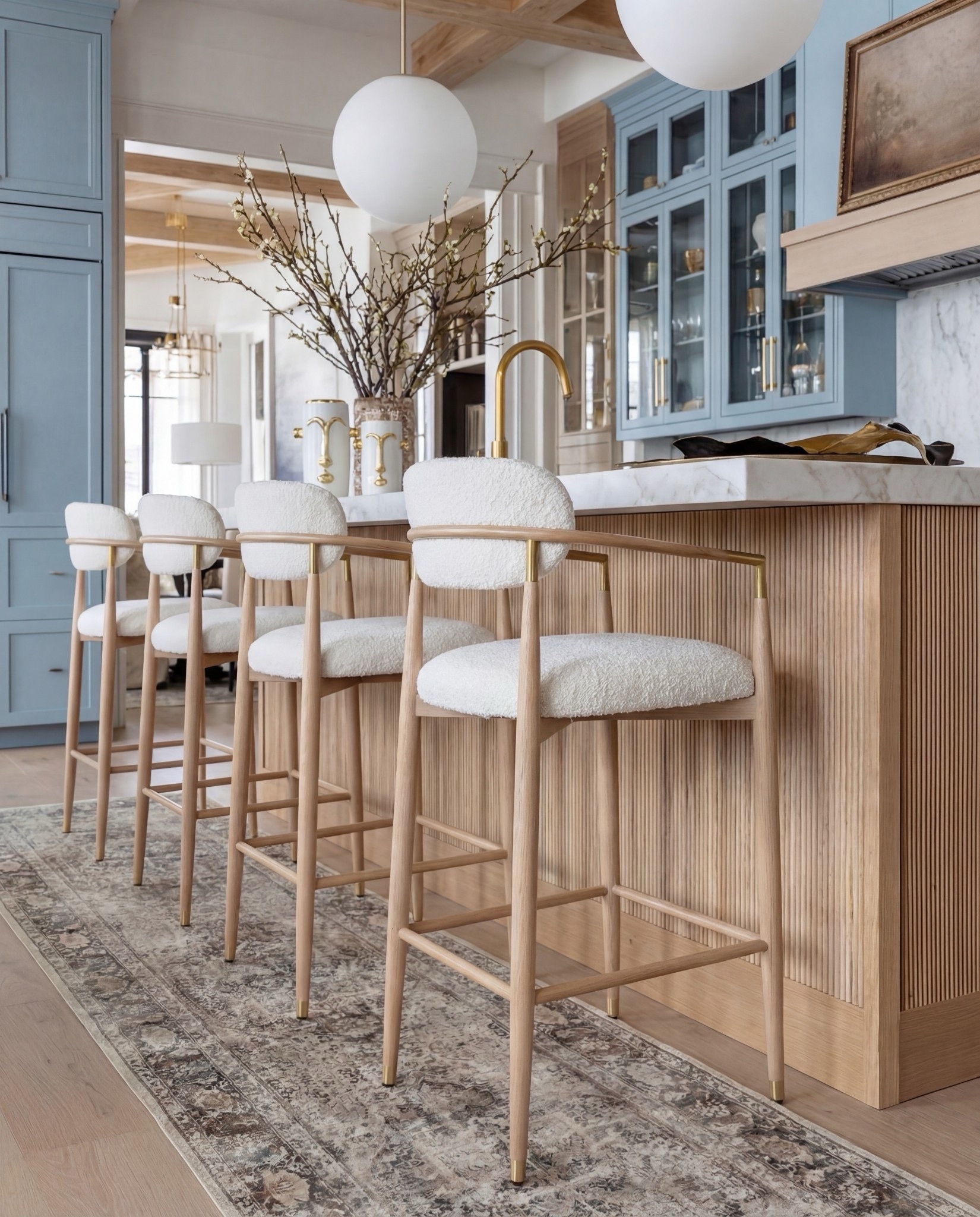 Shop the Look:
• Soft blue shaker-style kitchen cabinets
• White marble countertops & backsplash (warm veining)
• Slatted wood kitchen island paneling (light oak)
• White globe pendant lights (brass stem)
• Brass kitchen faucet + brass cabinet hardware
• Boucle counter stools with light wood frame
• Black gas range
• Vintage-style runner rugs (neutral taupe + faded pattern)
• Sculptural gold decorative bowls
• Wooden serving tray (warm walnut tone)
• White sculptural ceramic vases with dried florals
• Glass vase with branch arrangement

#LTKHome #LTKSpringSale #LTKSaleAlert