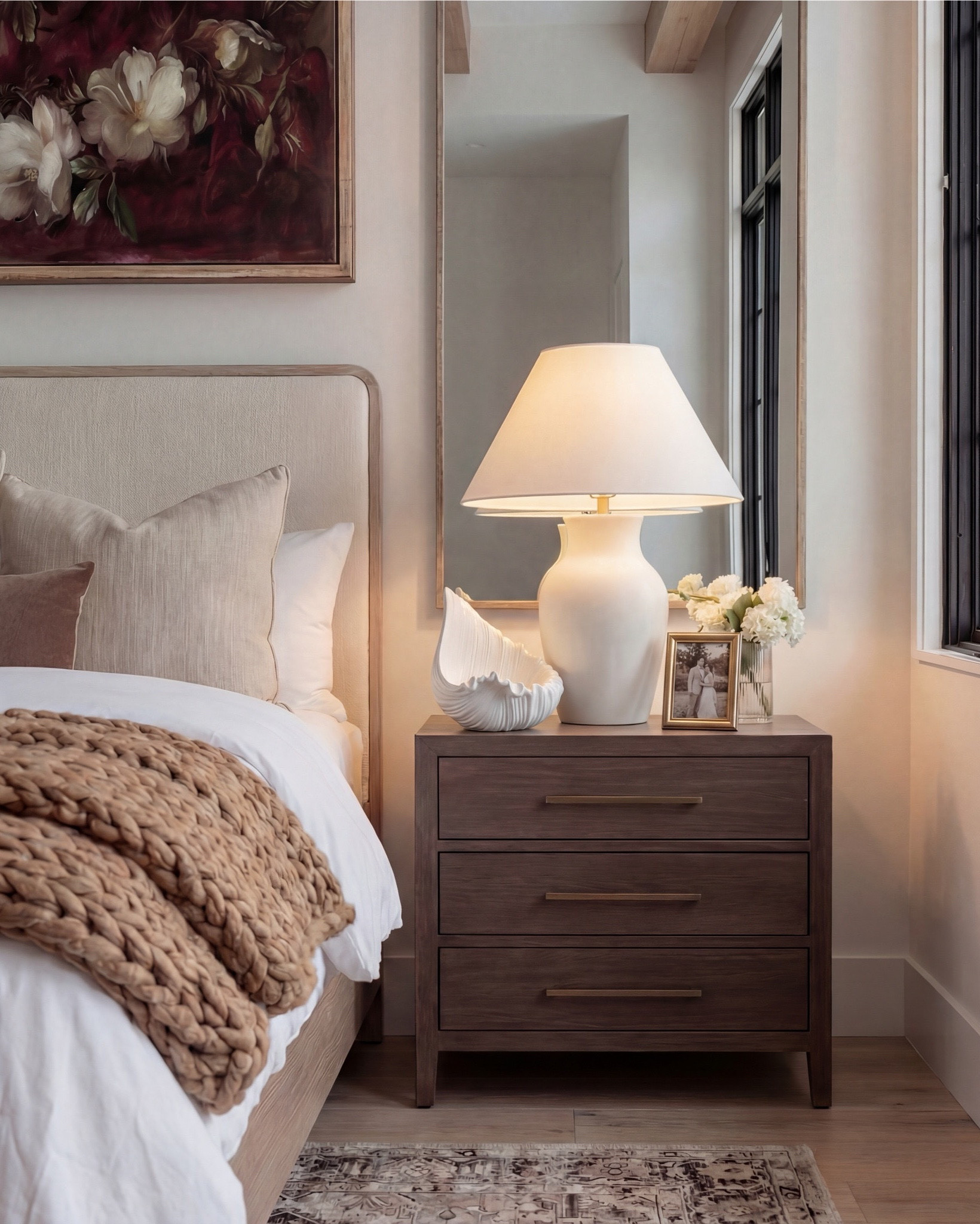 Shop the Look: Bedroom Refresh
• Upholstered bed frame (light neutral fabric)
• White cotton duvet cover + pillow shams
• Neutral patterned area rug
• Chunky knit throw blanket (warm beige)
• Woven knit poufs (foot-of-bed seating)
• Dark wood nightstands with brass pulls
• Sculptural white ceramic table lamps
• White tapered lamp shades
• Brass-framed rectangular mirrors
• Framed floral artwork (warm, moody tones)
• Neutral linen accent pillows
• Ceramic decorative bowl (white sculptural style)
• Small glass vase with white florals

#LTKhome #LTKsale #LTKstyletip