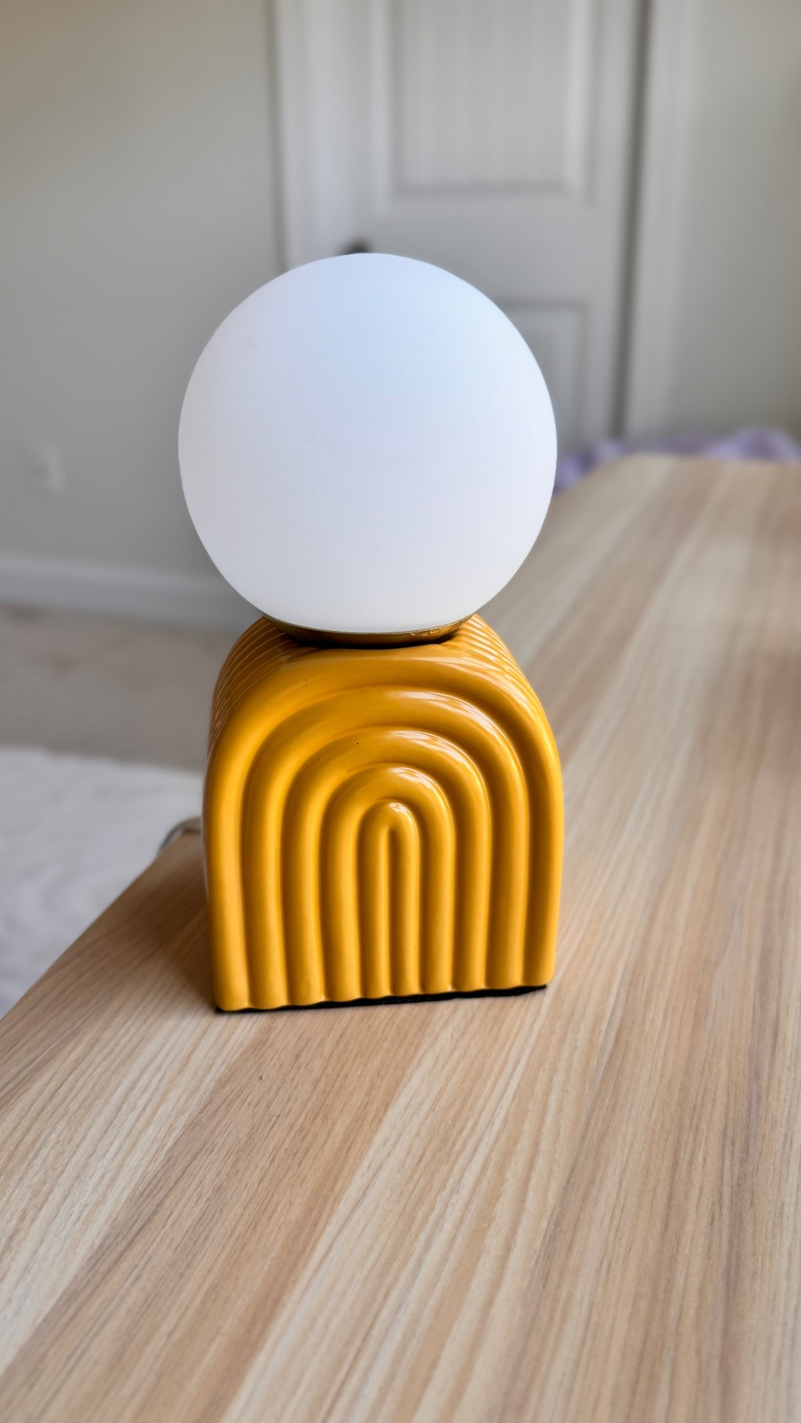 This modern accent lamp features a sculptural mustard yellow ceramic base with an arched ribbed design, topped with a soft white globe for a warm, diffused glow. Perfect for nightstands, desks, or styling shelves, it adds a playful yet elevated pop of color to any room.