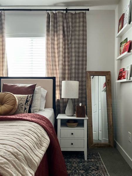 Gave our son’s bedroom a facelift and it feels so much better already. It’s amazing what styling can do, even without new paint or trim. His only request was to add red, his favorite color, so I built around the brick colored comforter. The rug has notes of that brick red spice color too, and paired with the plaid, it’s a pattern mixing dream. 
This nightstand was gifted to us and we are surprised by how much we actually like it! I wasn’t sure white would be right in the space but so far I’m into it. And the ribbed drawers and built-in charging station are my fave parts. 
Also loving that Studio McGee round gold throw pillow for a little elevated touch on the bed. 

Loloi rug
Bedroom styling
Bedroom furniture
Drapes
Upholstered twin headboard
Soft faux fur throw blanket
Round velvet throw pillow
Gray textured lamp with shade
Wall ledge shelves 
Black wall clock
Faux leather pillow covers
Full length mirror wood frame
Faux potted rubber tree
Wood tissue box cover
Constellation map print
White sheet set