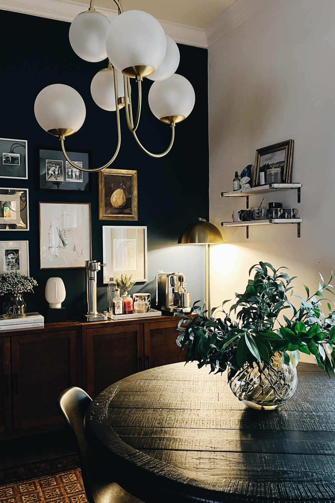 Loving my dining room view! The chandelier is no longer available and my table is an older style from RH. The wall color is Ben Moore’s Gentleman’s Gray which is the perfect navy! 
-
Moody dining room - dark dining room accent wall - marble wall shelves - gold shelf brackets - round black wood dining table - ribbed smoked glass vase - fake olive branches - dining room gallery wall - gold gallery wall frames - Studio McGee gold framed pear art - Britt Fabello art - vintage rug dining room - black Eames dining chairs - glass globe chandelier West Elm - H&M Home - Nespresso - Aarke carbonator - fake berries - coffee station decor 

#LTKsalealert #LTKhome