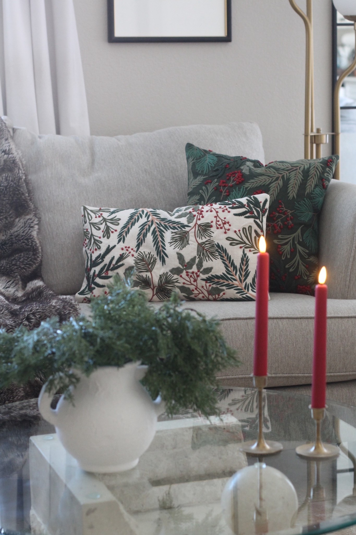 Cozy holiday living room decor featuring a neutral gray sofa styled with festive Christmas throw pillows in pine, greenery, and berry prints. A soft faux fur throw adds warmth, while elegant red taper candles bring classic Christmas charm. A white textured vase filled with winter greenery sits on a glass coffee table, creating a simple and sophisticated holiday centerpiece. This Christmas home decor look is perfect for anyone who loves modern, cozy, and nature-inspired holiday styling. Ideal inspiration for Christmas decorating ideas, holiday pillows, neutral Christmas decor, and festive living room styling.


#LTKHoliday #LTKSeasonal #LTKHome
