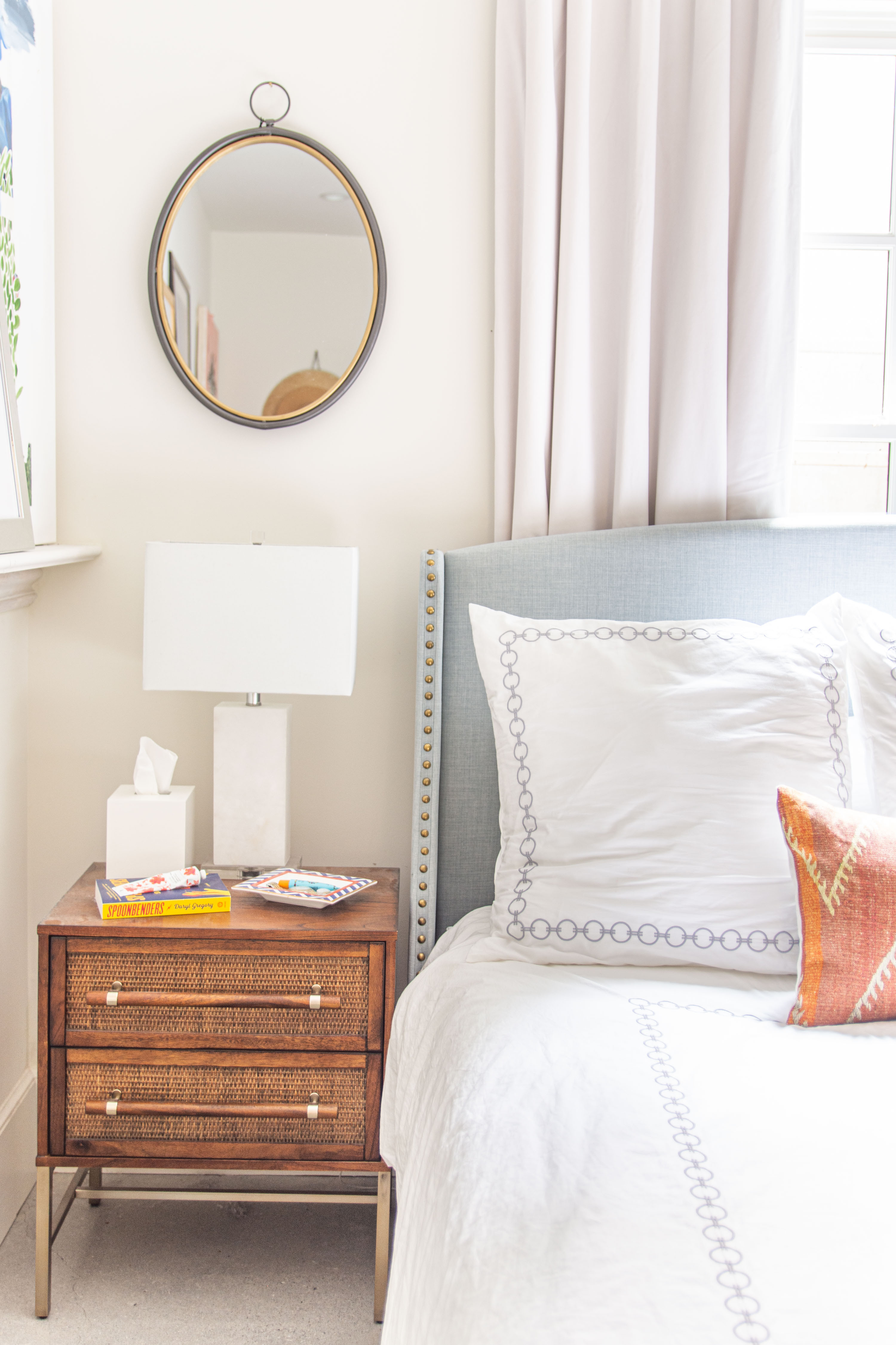 Bright and airy bedroom inspiration with timeless details. I styled this cozy bedside setup with a mid-century nightstand, modern white lamp, and neutral bedding accented with embroidered trim. The round wall mirror adds the perfect touch of contrast, while soft linen curtains frame the window for an inviting feel. Loving the layered pillows—classic white with subtle detailing paired with a warm, textured throw pillow for a pop of color. This look balances clean lines with natural textures, creating a chic yet comfortable retreat. 

 