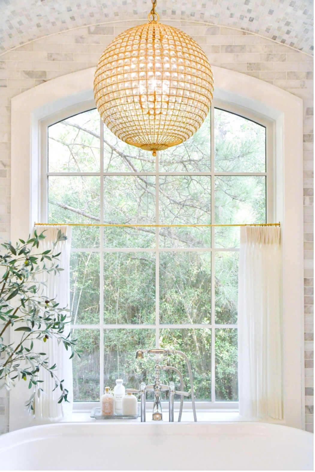 Chandelier in primary bathroom over bathtub with freestanding faucet 
Olive tree