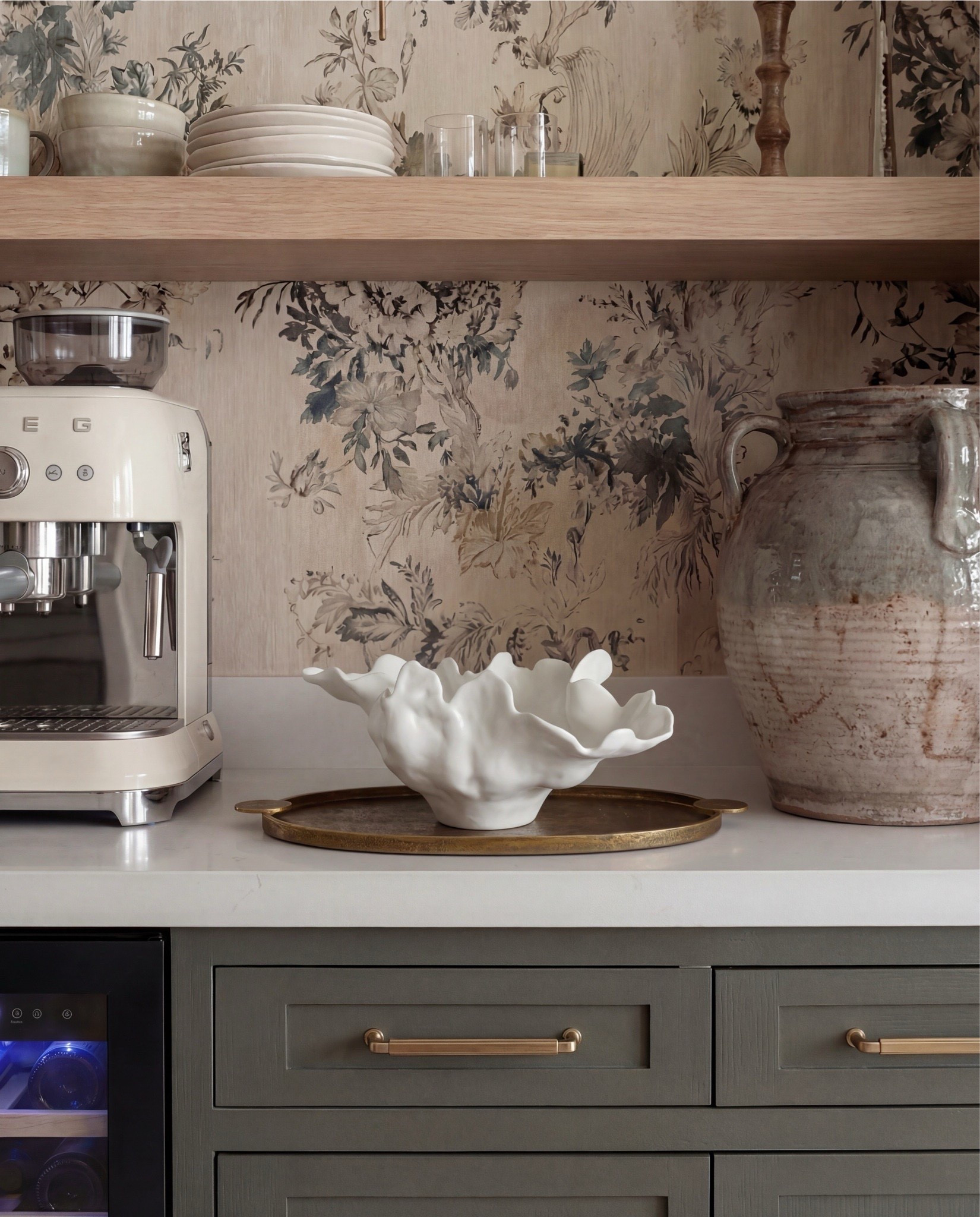 This cabinet moment feels warm, layered, and quietly collected. The muted green cabinetry sets a classic foundation, while the floral wallpaper adds softness and an almost vintage charm. Brass hardware and lighting bring in warmth, and the mix of fluted and glass-front cabinets keeps the wall feeling textured instead of heavy. Exposed wood ceiling beams and light oak floors ground the space with natural character.

The styling leans curated but livable—everyday pieces like glassware, coffee essentials, and ceramics are displayed intentionally, making the cabinet feel both functional and decorative.

Shop the Look:
• Muted green paneled cabinetry
• Brass cabinet pulls + drawer handles
• Fluted panel tall cabinets
• Glass-front upper cabinets
• Floral wallpaper (neutral botanical pattern)
• Brass wall sconce with white shade
• Light wood floating shelf
• White espresso machine
• Built-in beverage fridge
• Built-in wine fridge
• Clear wine glasses + stemware set
• Stacked ceramic plates + bowls
• Neutral ceramic mugs
• Sculptural ceramic bowl (organic shape)
• Large ceramic vase (earthy tones)
• Light wood flooring
• Vintage-style runner rug (soft neutral pattern)


#LTKSaleAlert #LTKHome