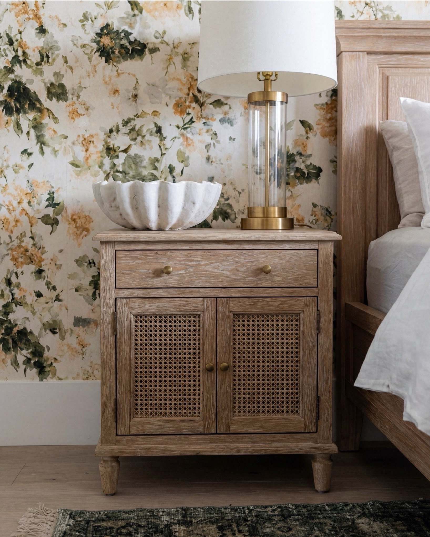 Shop the Look: Bedroom Refresh 
• Light oak panel bed
• Cream + green accent pillows
• Warm chunky knit throw
• Textured caramel cube ottomans
• Brass bedside lamps
• Fluted natural wood nightstands
• Green vintage-style rug
• Large white globe ceiling light
• Soft neutral pinch-pleat curtains
• Botanical floral wallpaper with soft gold + sage undertones

#LTKsale #LTKhome #LTKstyletip