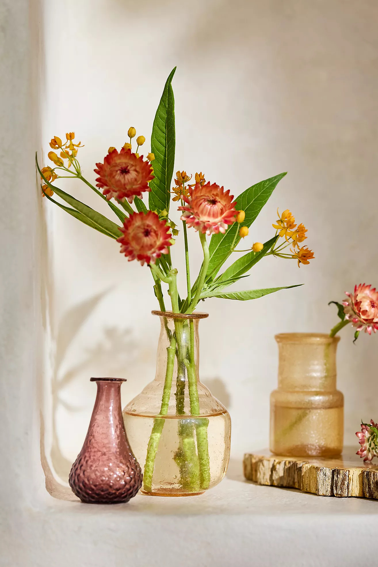 Three small glass bud vases in amber and blush tones holding a few flowers