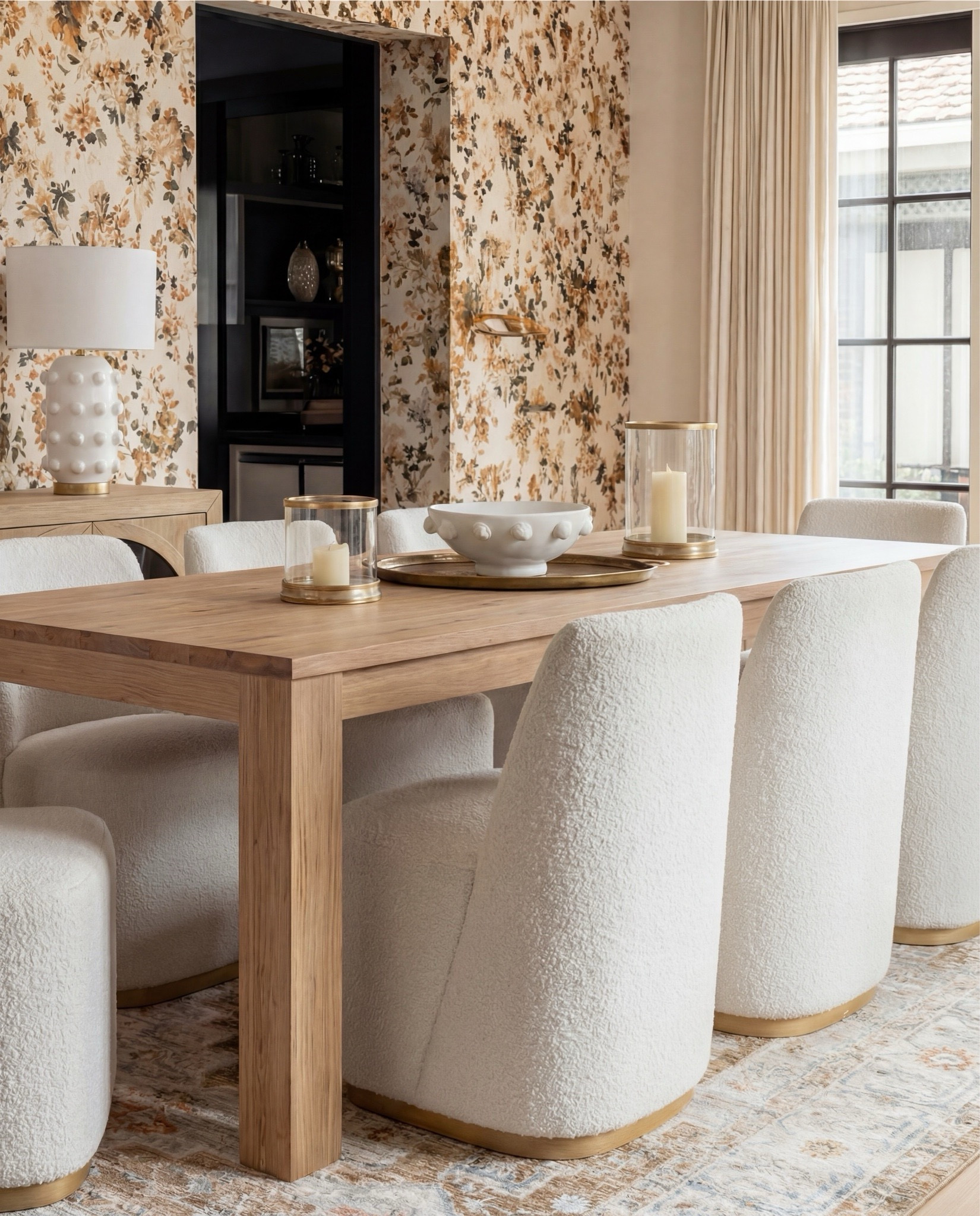 Shop the Look:
• Warm oak dining table
• Curved ivory dining chairs (brass base detail)
• Brass + globe statement chandelier
• Soft floral wallpaper (warm neutrals + terracotta)
• Oak sideboard with arched glass doors
• Textured ceramic table lamps + decor
• Neutral vintage-style area rug
• Gold trays + candle set
• White ceramic serving bowl

#LTKSaleAlert #LTKHome