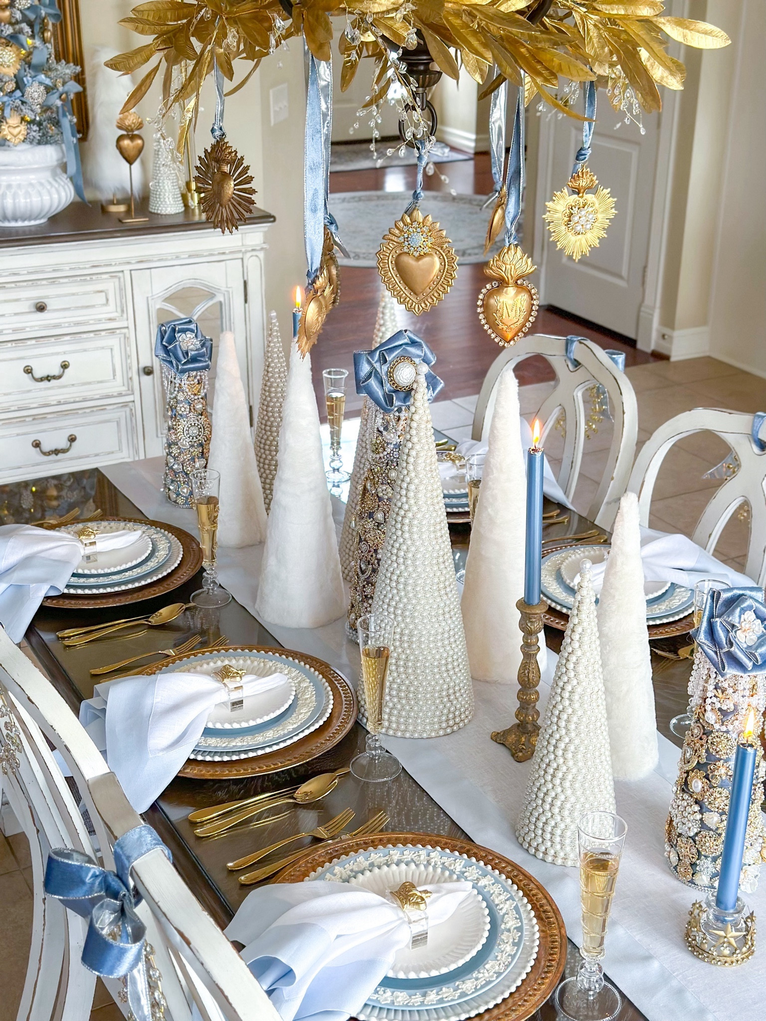 Shop my “Crowned with Love” Christmas Tablescape featuring gorgeous acrylic and gold crown napkin rings from Southern Tribute!

White fur trees, pearl trees, jewelry tree, brooch tree, gold sacred hearts, Milagro heart, champagne flutes, tabletop tree, Wedgwood plates, queensware, gold bay leaf garland, Christmas table ideas, Christmas entertaining, blue and white Christmas, light blue table linens