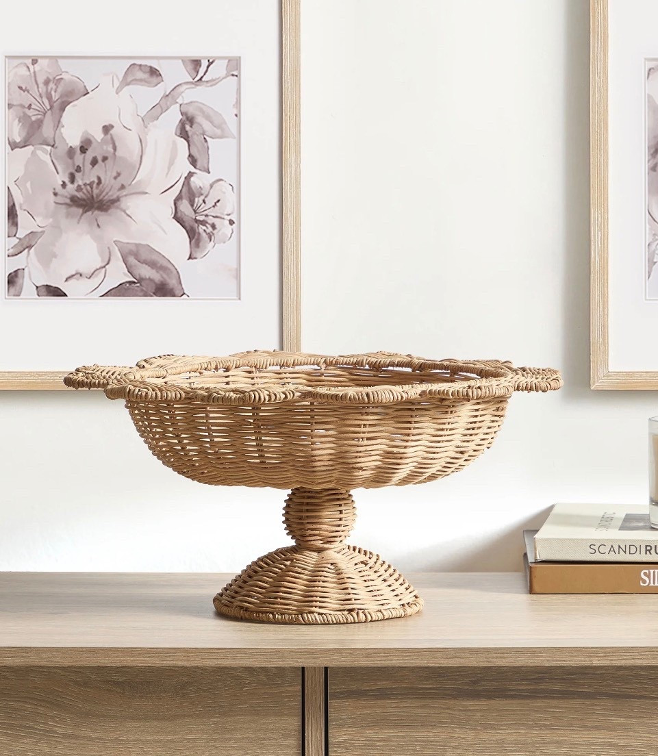 The My Texas House Rattan Scalloped Decorative Bowl brings an easy summertime charm to your home with its woven rattan design and eye-catching scalloped edge. This 16-inch by seven-inch bowl is a simple way to add texture and warmth to coffee tables, kitchen counters, and dining room displays. Its raised pedestal base gives it a graceful shape that works well for holding faux fruit, florals, or seasonal accents. The natural rattan adds a light and airy look that blends beautifully with farmhouse and coastal inspired decor. You can style it on its own as a statement piece or pair it with other summer decorations to create a coordinated display. The My Texas House Rattan Scalloped Decorative Bowl is a lovely choice for refreshing your space with a touch of natural style.