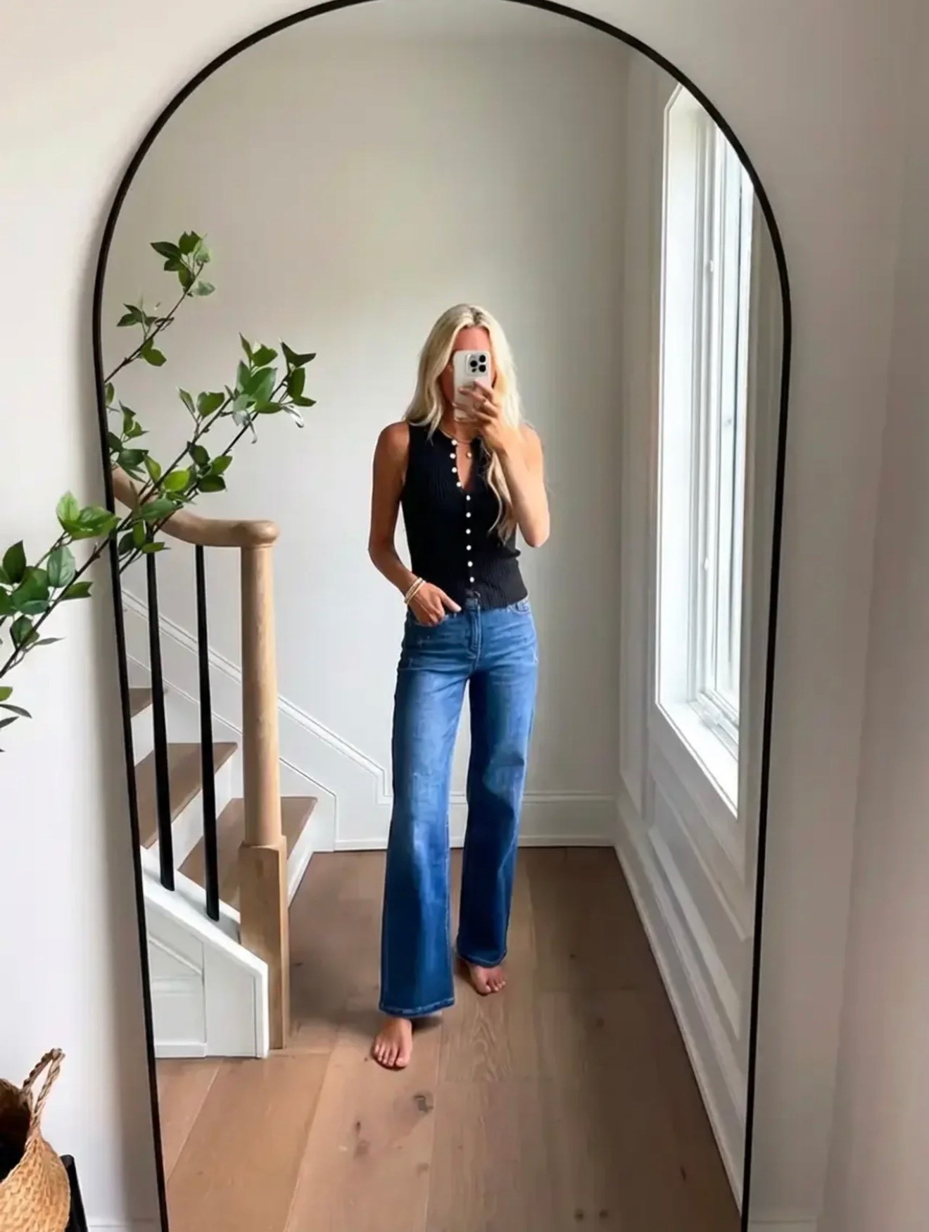 A minimalist lifestyle fashion mirror selfie in a bright modern home. A woman with long blonde hair stands barefoot in front of a large arched black-framed mirror. She is wearing a sleeveless black button-front knit top paired with high-waisted medium-wash straight leg jeans. The interior features light natural oak floors, white walls, a staircase with light wood railing and black balusters, and soft natural light streaming through a tall window. A touch of greenery from a plant branch adds warmth. The aesthetic is modern coastal minimalism, effortless everyday style, clean luxury lifestyle photography, soft natural lighting, editorial Instagram fashion aesthetic.

Caption

Effortless classics never miss. 🖤
Denim + a simple top = always the right choice.

Hashtags

#EffortlessStyle
#DenimStyle
#ClassicOutfit
#SimpleChic
#MinimalStyle
#ModernStyle
#CasualChic
#EverydayOutfit
#StyleInspoDaily
#TimelessFashion
#OOTDInspo
#MirrorSelfieStyle
#DenimLook
#NeutralStyle
#MinimalFashion
#ChicAndSimple
#CoastalStyle
#CasualLuxury
#EverydayStyle
#StyleInfluencer

#LTKdayinmylife #LTKSpringSale #LTKgrwm