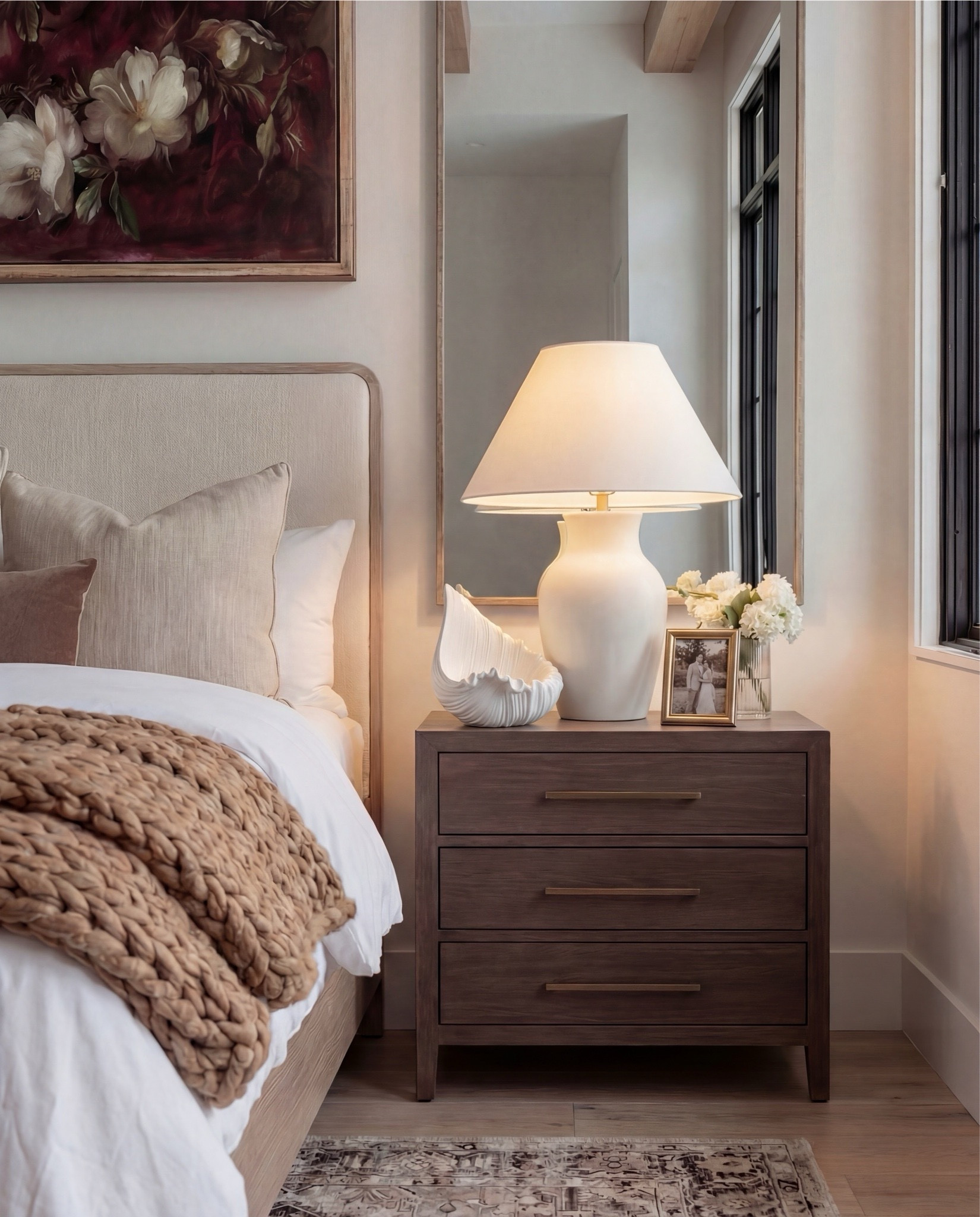 Shop the Look: Bedroom Refresh
• Upholstered bed frame (light neutral fabric)
• White cotton duvet cover + pillow shams
• Neutral patterned area rug
• Chunky knit throw blanket (warm beige)
• Woven knit poufs (foot-of-bed seating)
• Dark wood nightstands with brass pulls
• Sculptural white ceramic table lamps
• White tapered lamp shades
• Brass-framed rectangular mirrors
• Framed floral artwork (warm, moody tones)
• Neutral linen accent pillows
• Ceramic decorative bowl (white sculptural style)
• Small glass vase with white florals

#LTKSaleAlert #LTKHome