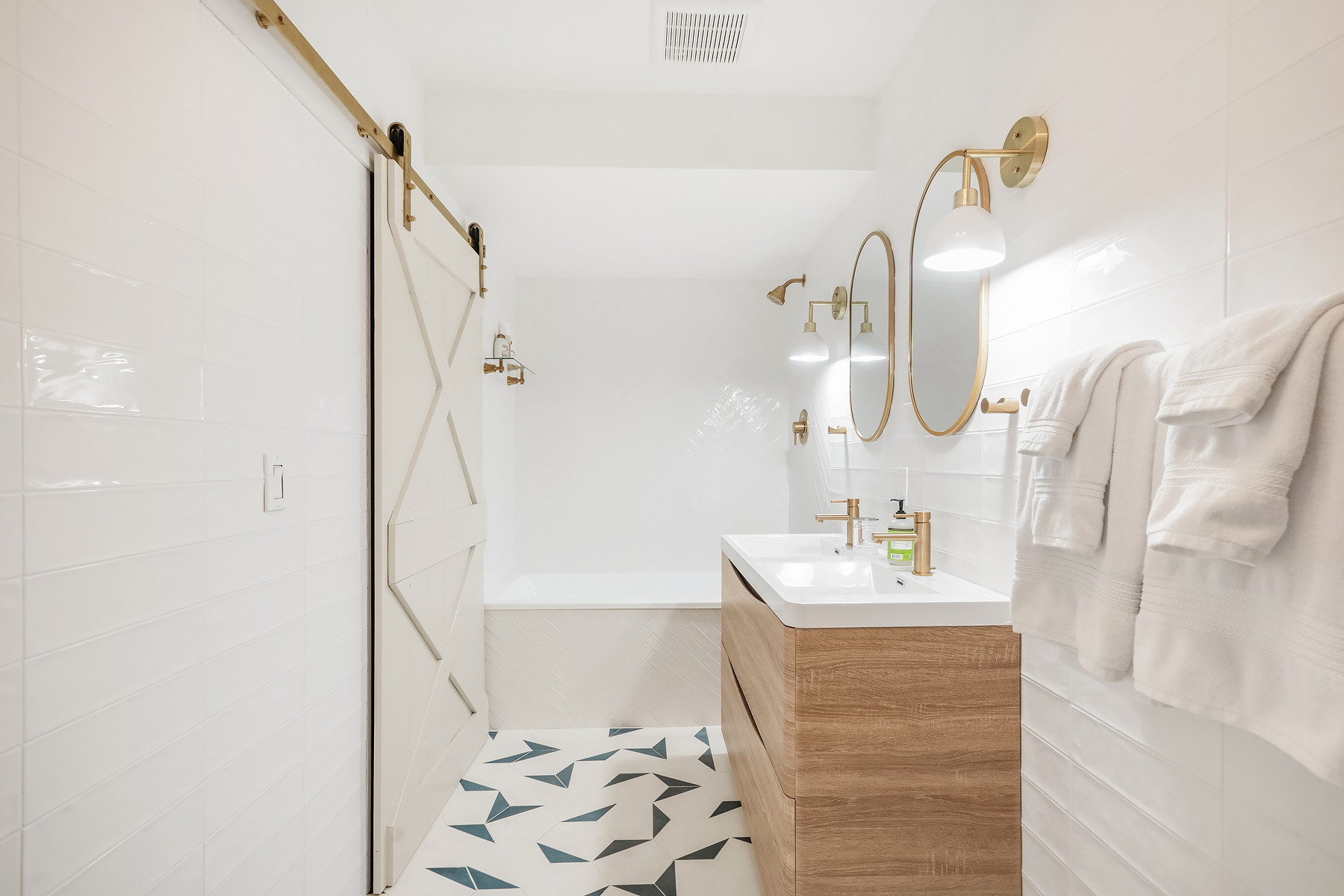 Bathroom with a wood vanity, brass fixtures, round mirrors, and white wall tile. We used the same tile on both the front of the tub and the tub surround. Added a sliding door and geometric floor tile. Linking exact and similar pieces here.

#LTKHome #LTKSaleAlert