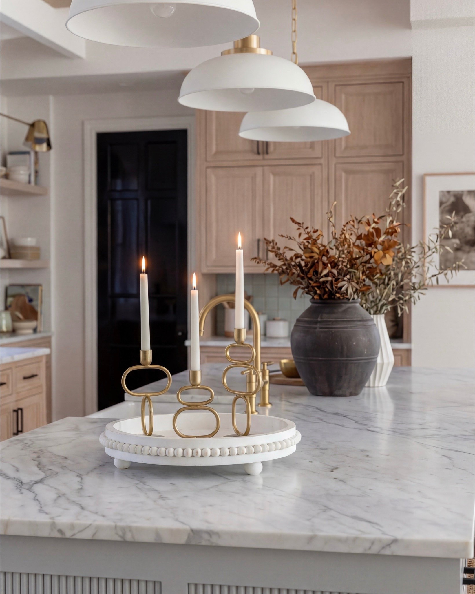 Shop the Look:
• Light natural wood kitchen cabinetry
• Soft blue fluted kitchen island
• White marble countertop (waterfall-style island top)
• Brass gooseneck kitchen faucet
• White dome pendant lights with brass details
• Cane-back counter stools with wood frames
• Matte black range and oven with brass hardware
• Pale blue tile backsplash
• Vintage-inspired runner rug (blue/neutral tones)
• Ceramic decorative vase (charcoal or earthy tone)
• Faux or dried olive branches / greenery
• Sculptural blue ceramic bowl
• Brass candle holders with taper candles
• White round pedestal tray (beaded edge style)
• Wood cutting boards (layered for display)
• Brass decorative tray

#LTKHome #LTKSaleAlert