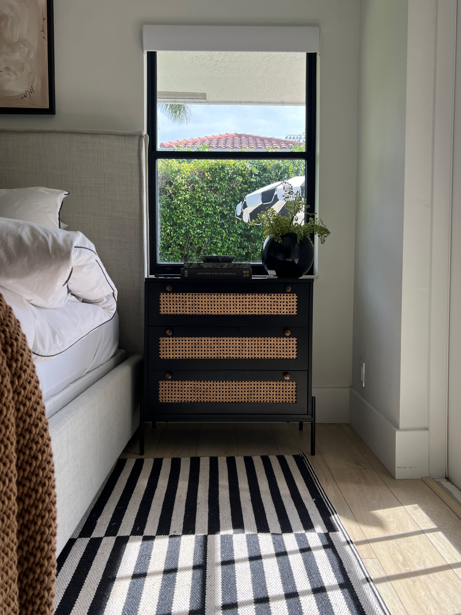 Nighstand decor! 
Black nightstand 
Faux fern 
Striped black and white rug 
Upholstered bed 
Throw blanket 
Bedroom decor 
#meandmrjones 

#LTKunder50 #LTKunder100 #LTKhome