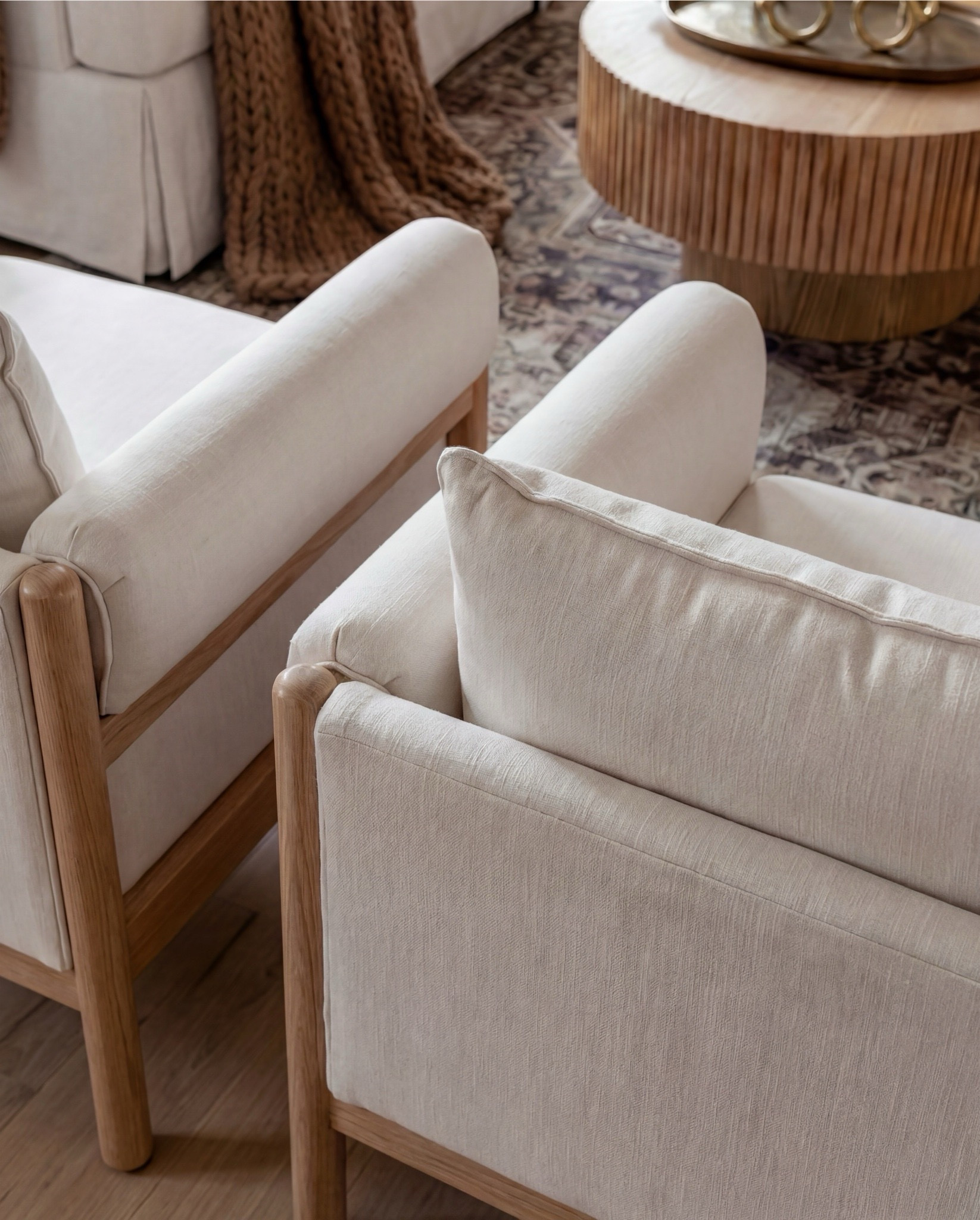 Shop the Look:
• White upholstered sofa (clean-lined, low profile)
• White upholstered armchairs (pair)
• Light wood round coffee table (fluted or ribbed base)
• Neutral vintage-style area rug (muted brown and beige tones)
• Marble fireplace surround
• Black fireplace insert
• Large framed landscape wall art (soft blue and neutral tones)
• Brass wall sconces (pair, globe style)
• White globe pendant light with brass detail
• Natural wood ceiling beams
• Light wood flooring

Coffee Table Styling:
• Large white ceramic vase (rustic sculptural style)
• Decorative hardcover books (neutral covers)
• Gold abstract heart sculpture
• Brass oval tray
• Decorative brass object (sculptural accent)

Sofa Styling:
• Neutral throw pillows (warm beige)
• Chunky knit throw blanket (camel or warm brown)

Media Console Area:
• Light wood sideboard / media console (carved front detail)
• Brass cabinet knobs
• Black figurine sculptures (musician figures, set of three)
• Brown ceramic vase
• Dried branches / minimalist floral stems
• Brass decorative tray

#LTKHome #LTKSaleAlert