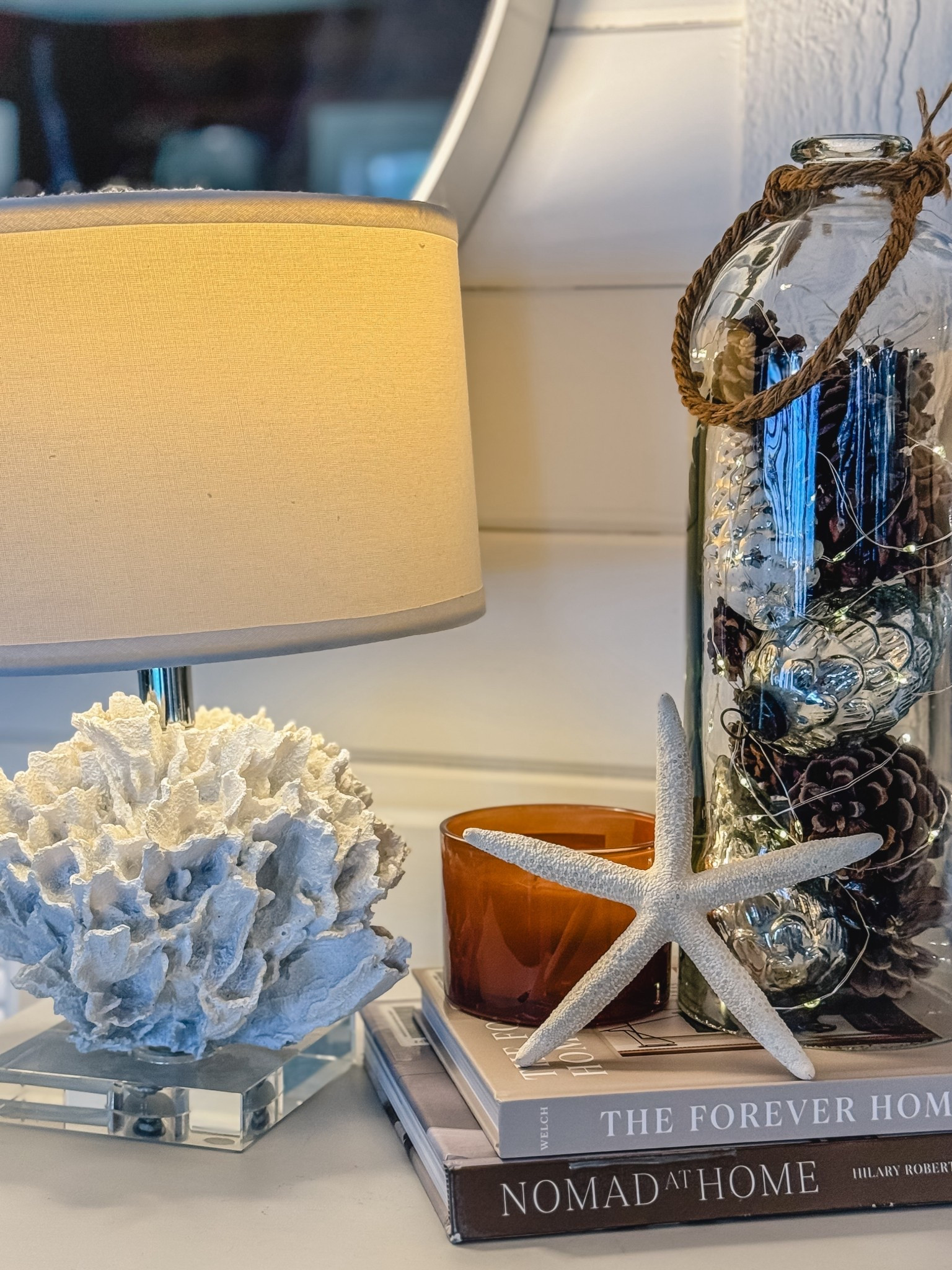 Transitioning from Christmas Decor to winter whites and browns.  With the decorations down, it feels bare and dark. So I filled this glass cloche with foraged pine cones, mercury glass cones and fairy lights. Adding a candle for scent still gives it a woodsy smell. The dried star dish and coral lamp add a coastal vibe  

#LTKhome #LTKwinter #LTKstyletip