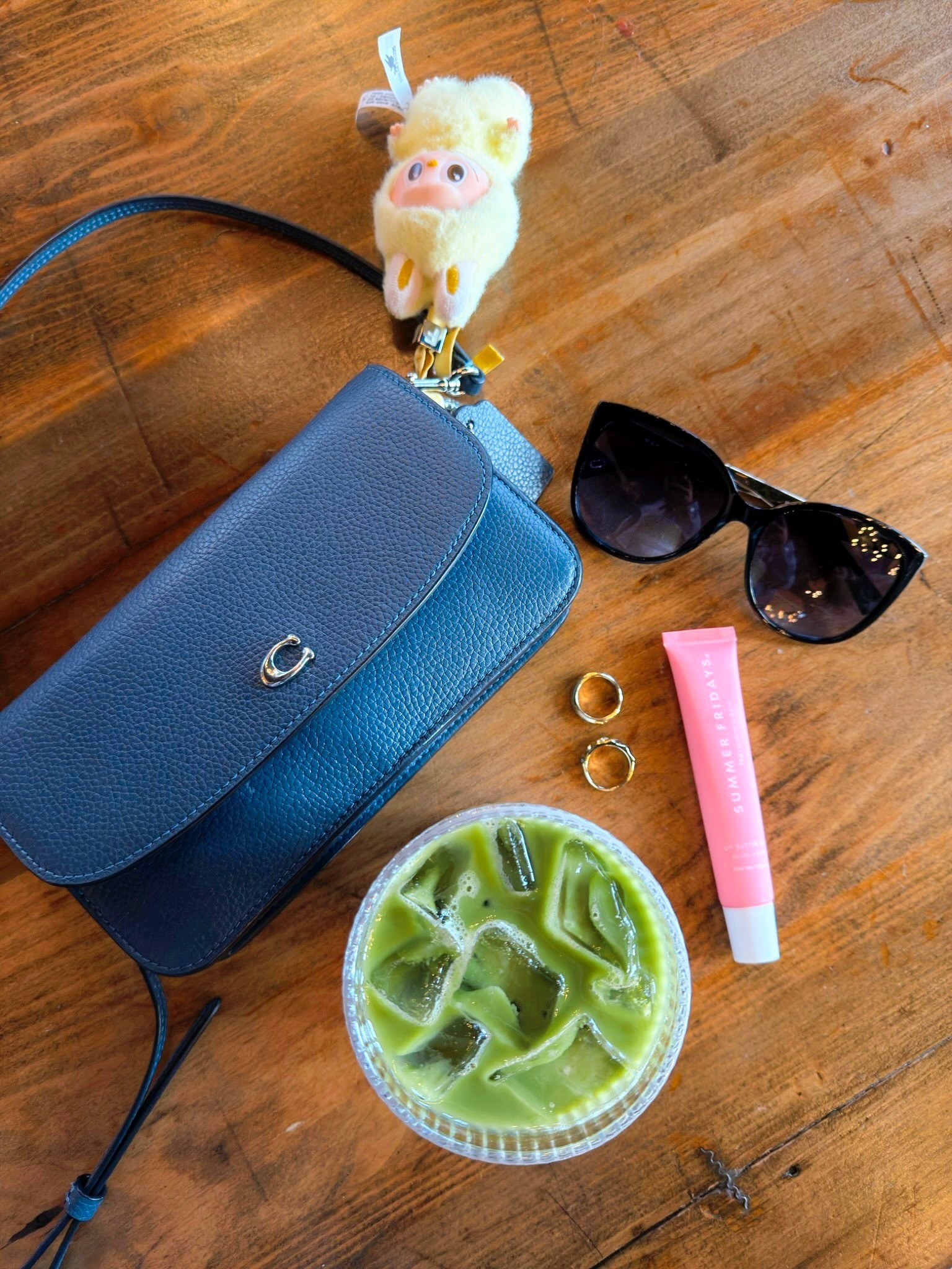 Coffee shop essentials for your aesthetic photo dreams. Blue leather Coach crossbody bag, gold wavy rings, black cat eye sunglasses, Summer Fridays Pink Sugar lip balm, clear class cups, labubu pin for love pendant keychain.

#LTKdayinmylife #LTKHome #LTKTravel