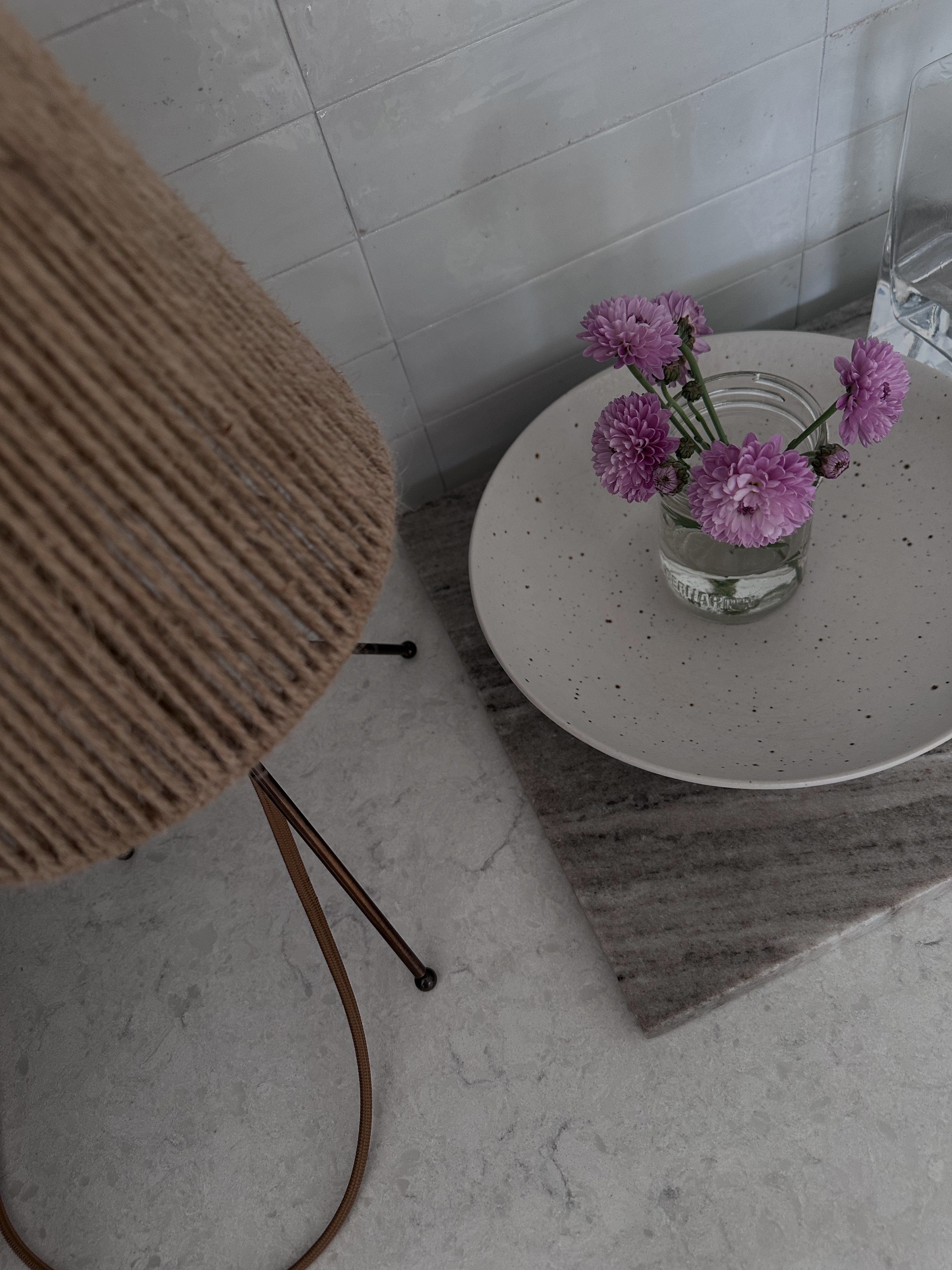 Neutral modern organic kitchen styling moment featuring a woven rattan table lamp, marble countertop, speckled ceramic tray, and fresh purple mini mums in a clear glass vase. Loving the mix of warm natural textures with cool stone and soft florals — simple, organic home decor details that make everyday spaces feel elevated and cozy. 

 #LTKdayinmylife #LTKHome