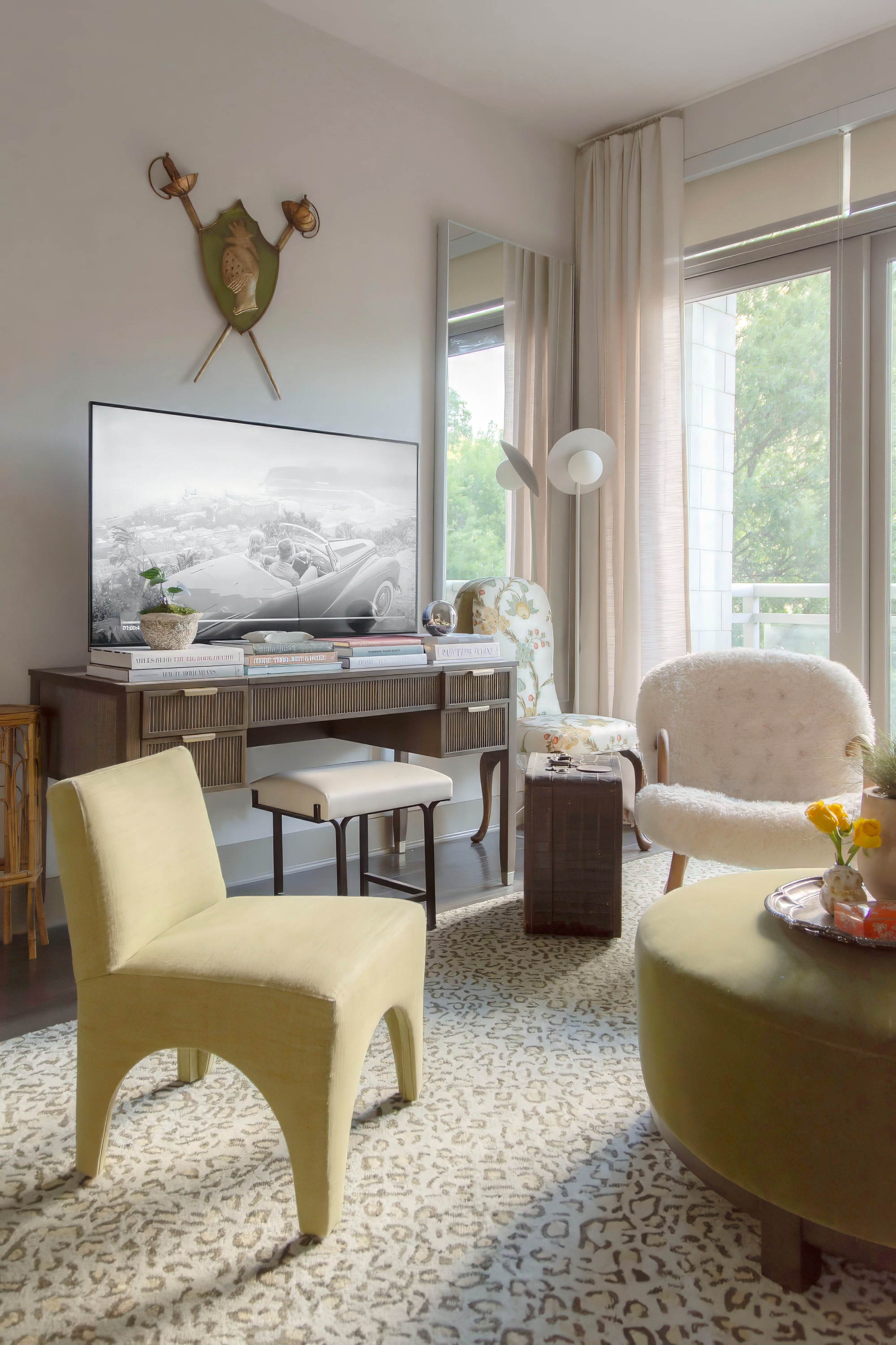 Modern eclectic living room with layered textures and cozy neutral tones. This space combines a boucle accent chair, vintage-inspired floral upholstery, and a curved olive ottoman for a soft yet elevated vibe. The leopard patterned area rug anchors the room and adds subtle personality, while natural light filters through sheer curtains for an airy feel. A mid-century style console doubles as a TV stand and desk, styled with design books and decor. Perfect mix of modern furniture and timeless accents for a chic apartment living room makeover. 

 