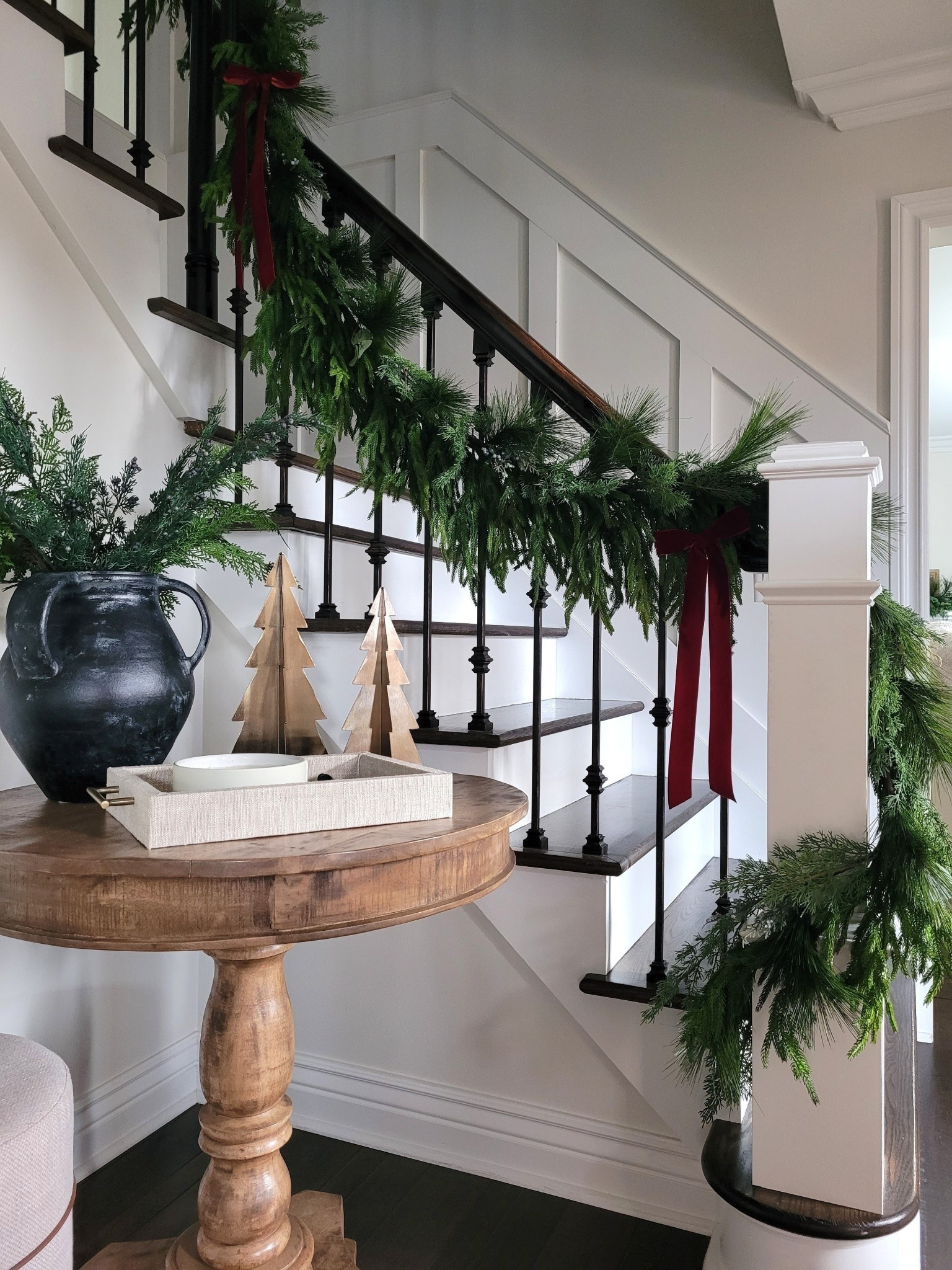 Simple holiday entryway Christmas decor with layered garland and Amazon velvet ribbon, mud cloth ottoman, round console table,  staircase

#LTKHome #LTKHoliday