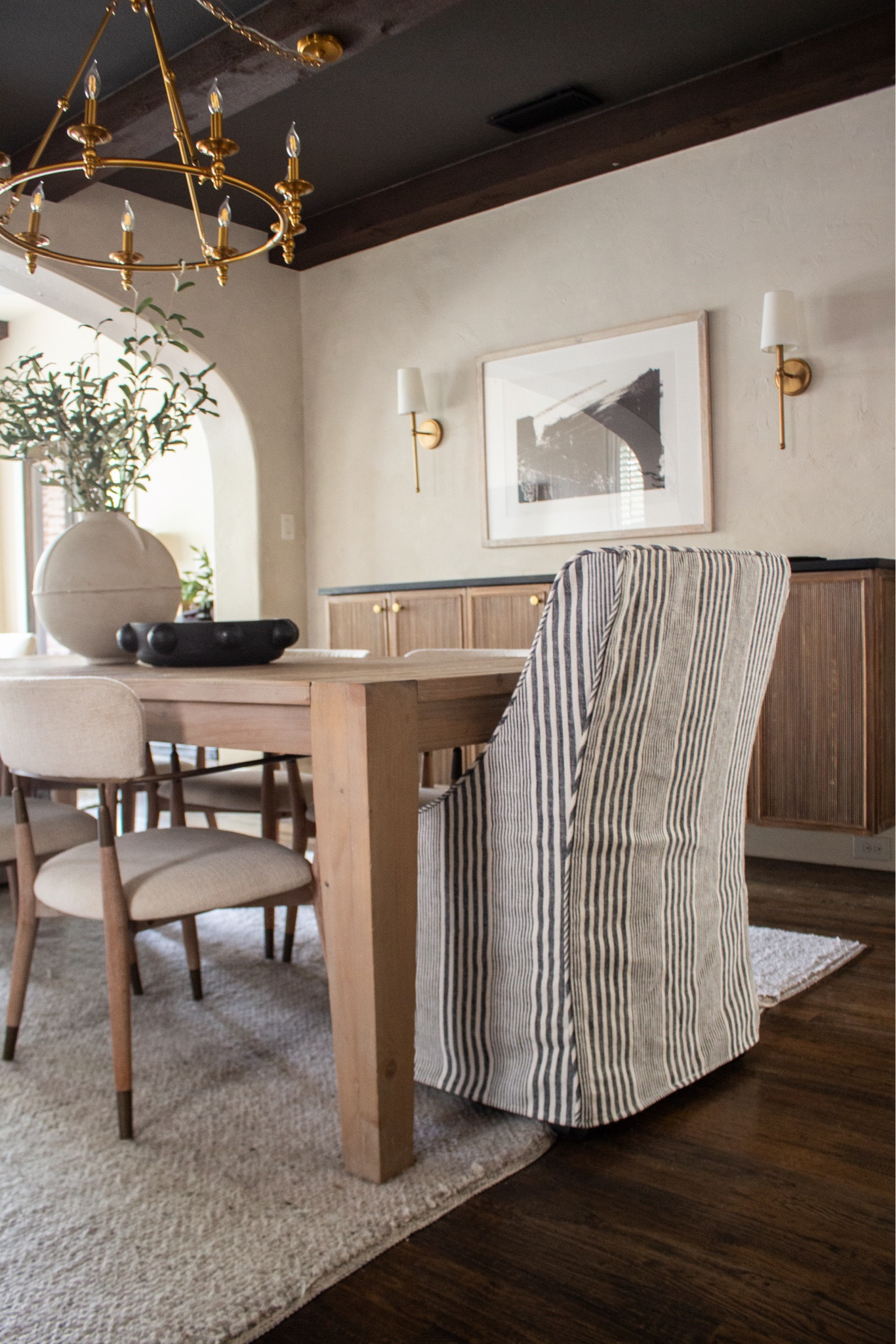 Warm wood tones + classic stripes will always feel timeless in a dining space. I love mixing clean lines with soft texture to keep it feeling elevated but still cozy for everyday family dinners. This space is the perfect blend of modern traditional and organic warmth.

dining room inspiration, modern traditional dining room, striped dining chairs, wood dining table, neutral dining room decor, brass chandelier, wall sconces, dark ceiling beams, cozy home decor, timeless interior design

#LTKdayinmylife #LTKHome #LTKSeasonal