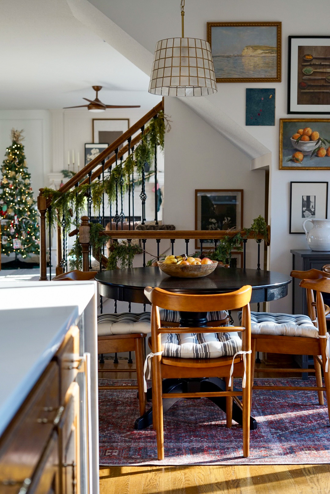 A cozy Christmas breakfast nook setup with wooden chairs around a black table, plus a pretty pendant light hanging above. The walls are filled with art, and there's a vintage style rug that pulls it all together. 

 

#LTKHoliday #LTKHome