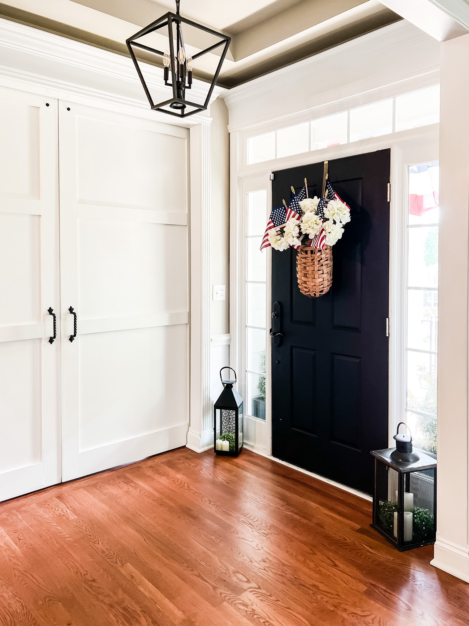 Simple patriotic front door decorating with a hanging basket for flowers. Fill it with faux hydrangeas all summer long. Then, tuck in some large American flags for patriotic US summer holidays like Memorial Day or 4th of July. Place large black candle lanterns by the door for balance. 

#LTKHome #LTKStyleTip #LTKSeasonal