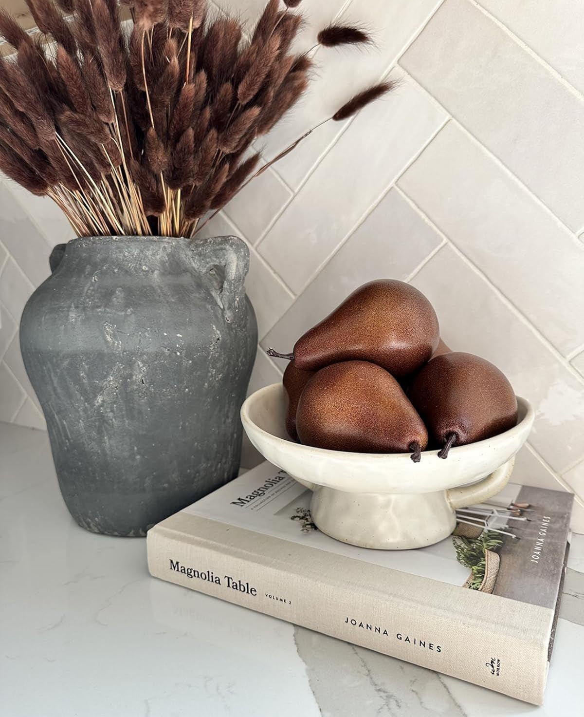 Autumn vignette. Fall kitchen decor. Realistic brown pears. Faux fruit. Affordable home decor. Autumn kitchen decor. Grey vase, brown bunny tail stems, cream pedestal bowl, magnolia cookbook. | Amazon (US)