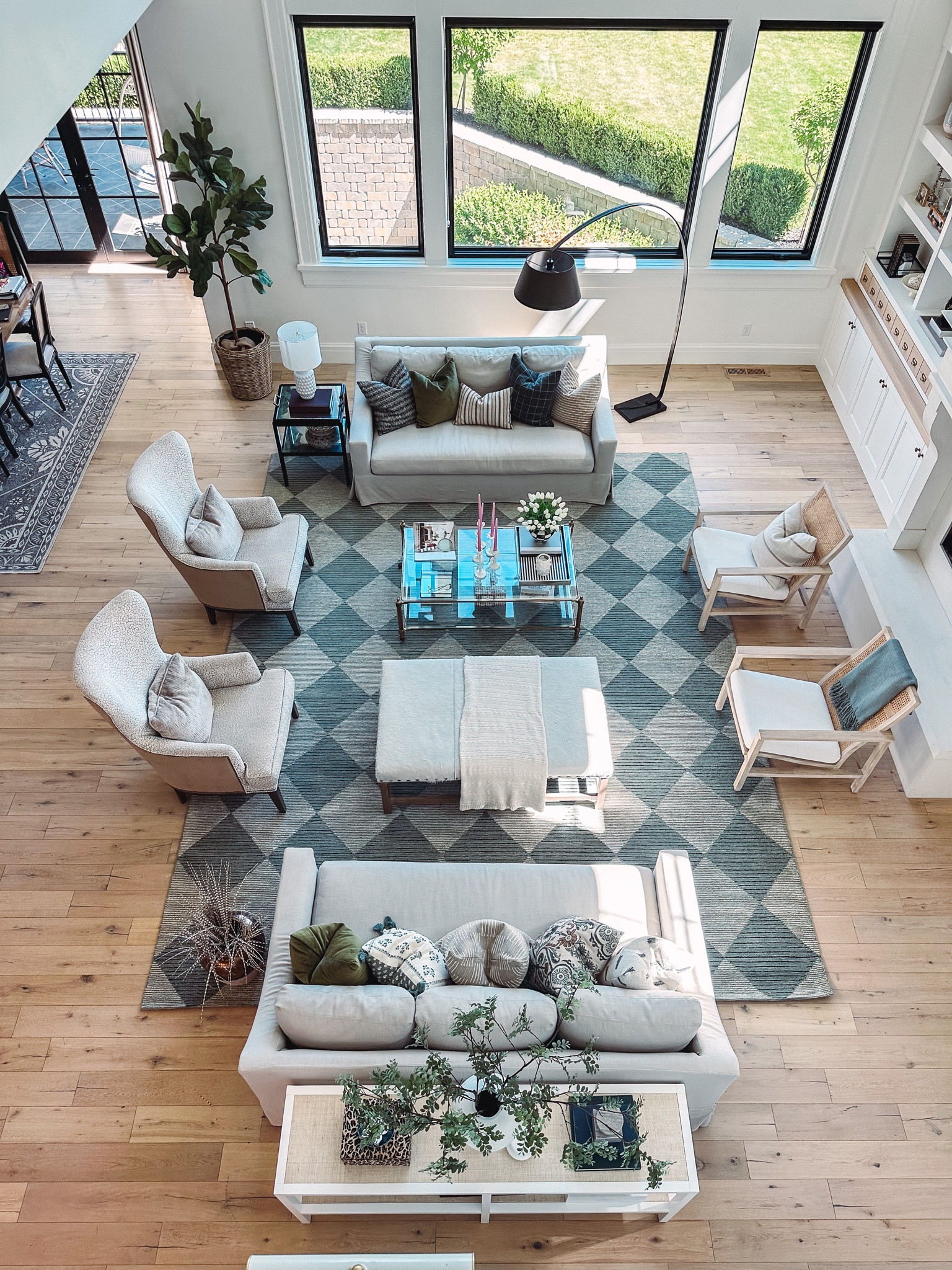Living room details with wool high pile checkered rug, bench sofas, brass ans glass coffee table, ottoman, ans cane back chairs 
